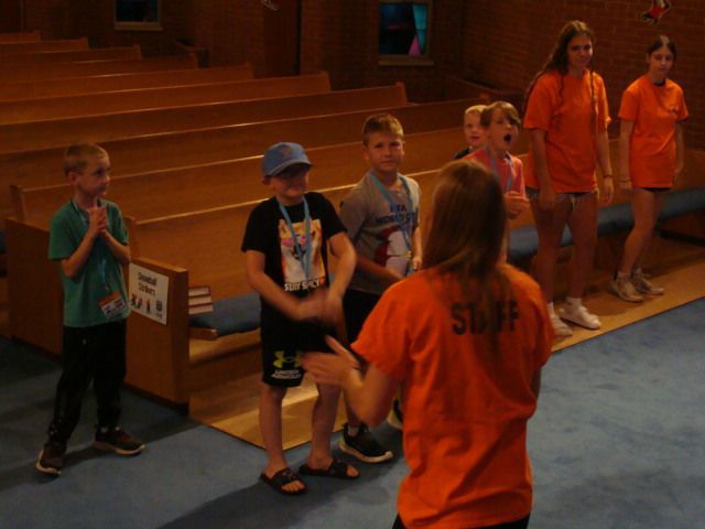 Children stand in a church aisle with orange-shirted staff during a group activity.