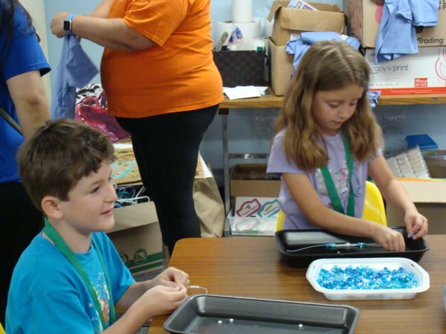 Two children at a table making crafts with blue beads in a classroom