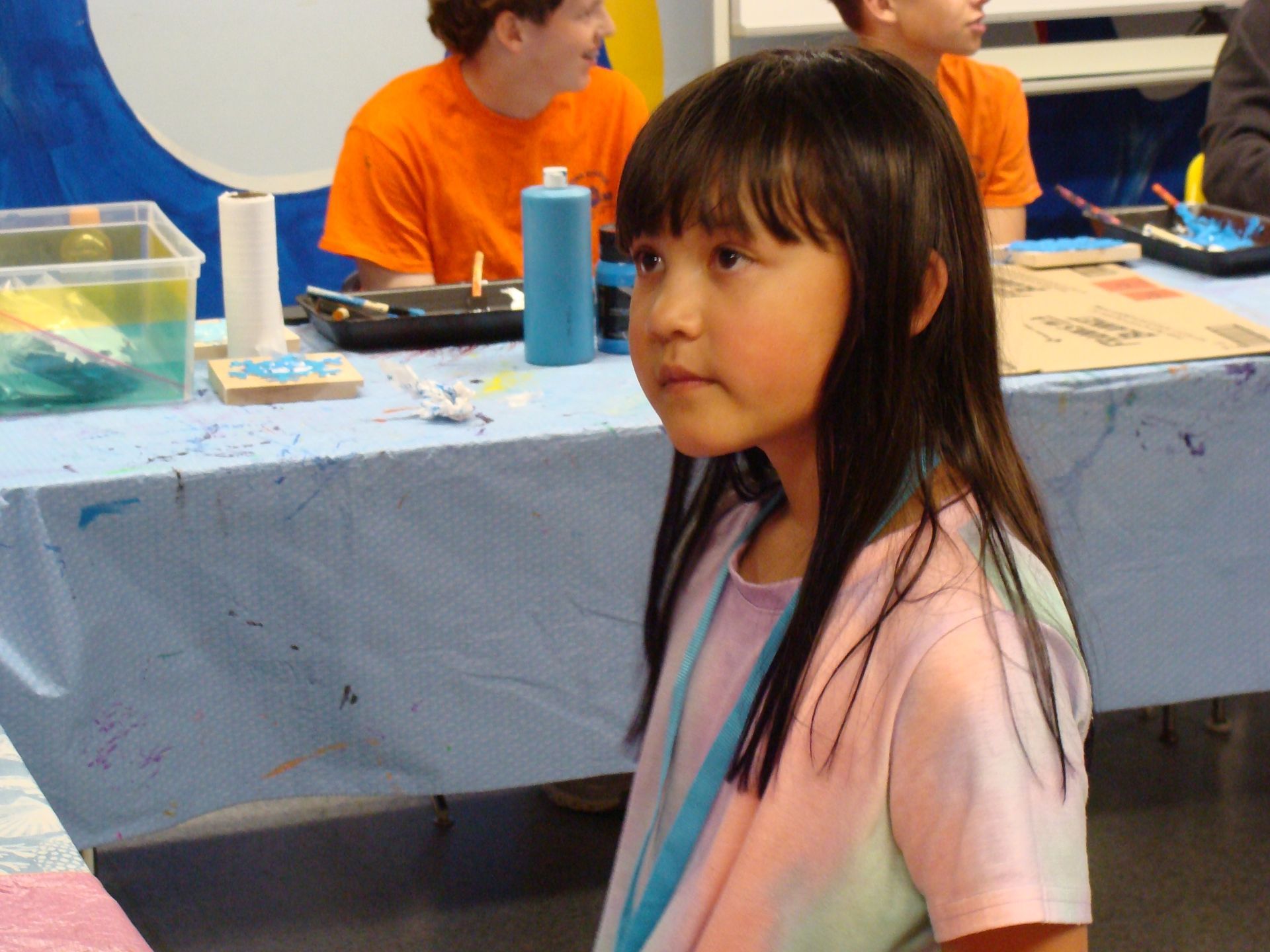 Child in a pink shirt standing by a table with art supplies in a classroom