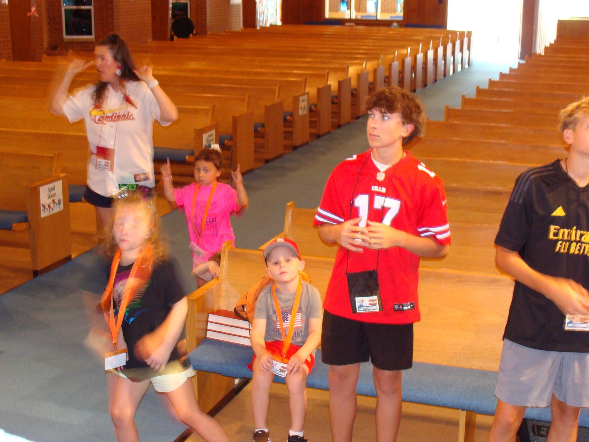 Children standing in a church aisle, with one in a red jersey holding a number 17 sign