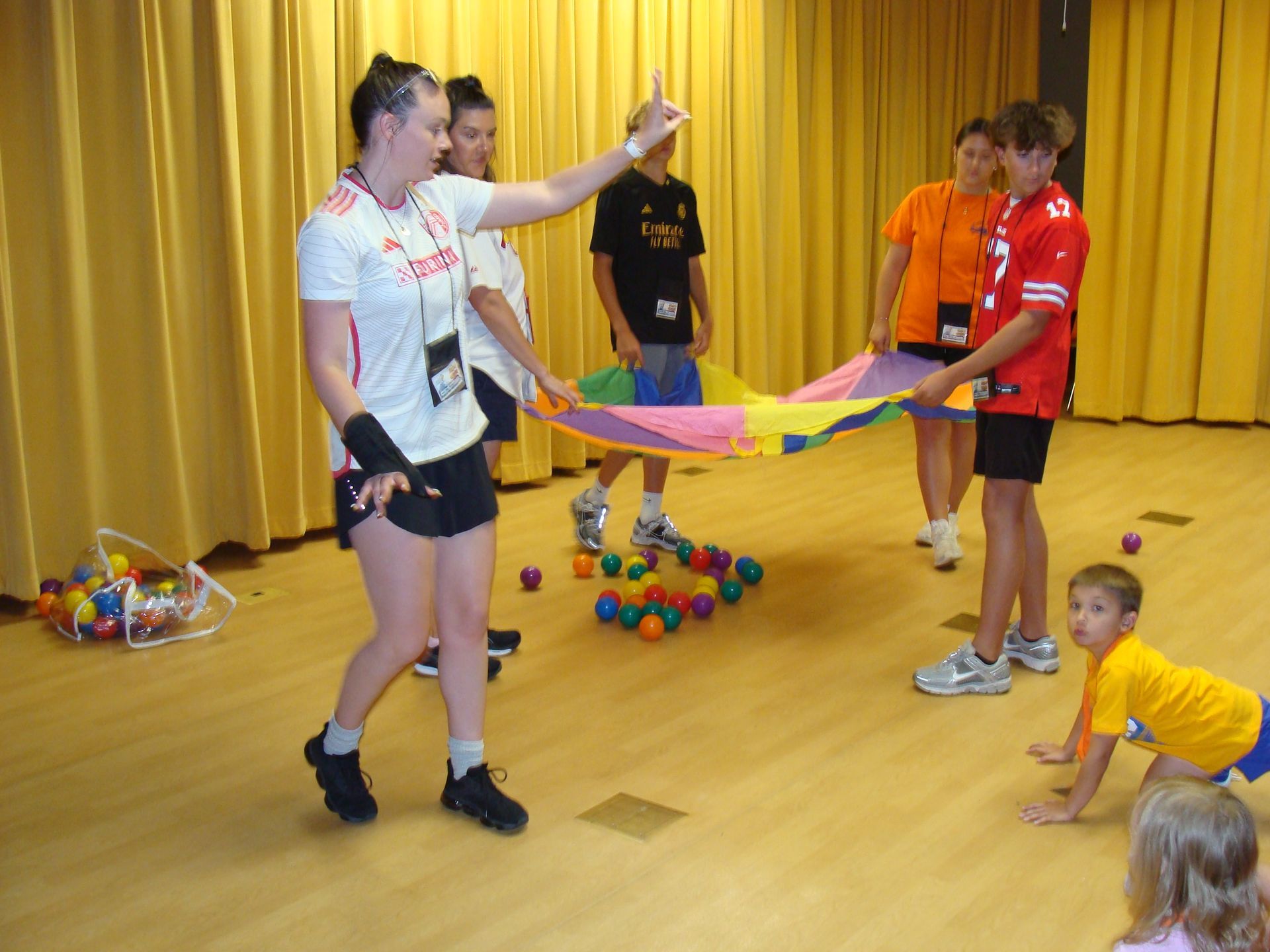 People holding a colorful parachute in a hall, with children playing around them