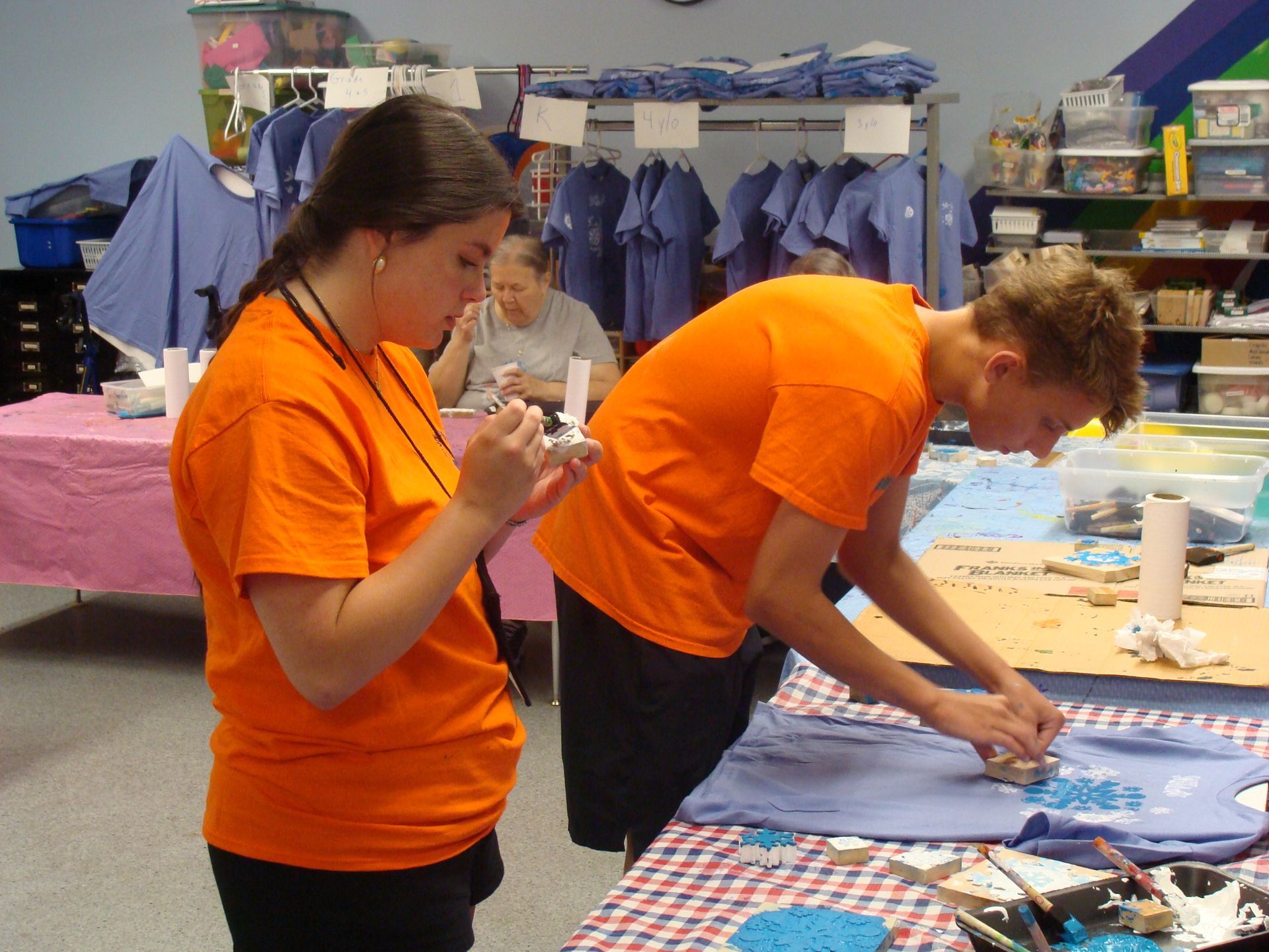 People in orange shirts working at a craft table in a classroom or workshop