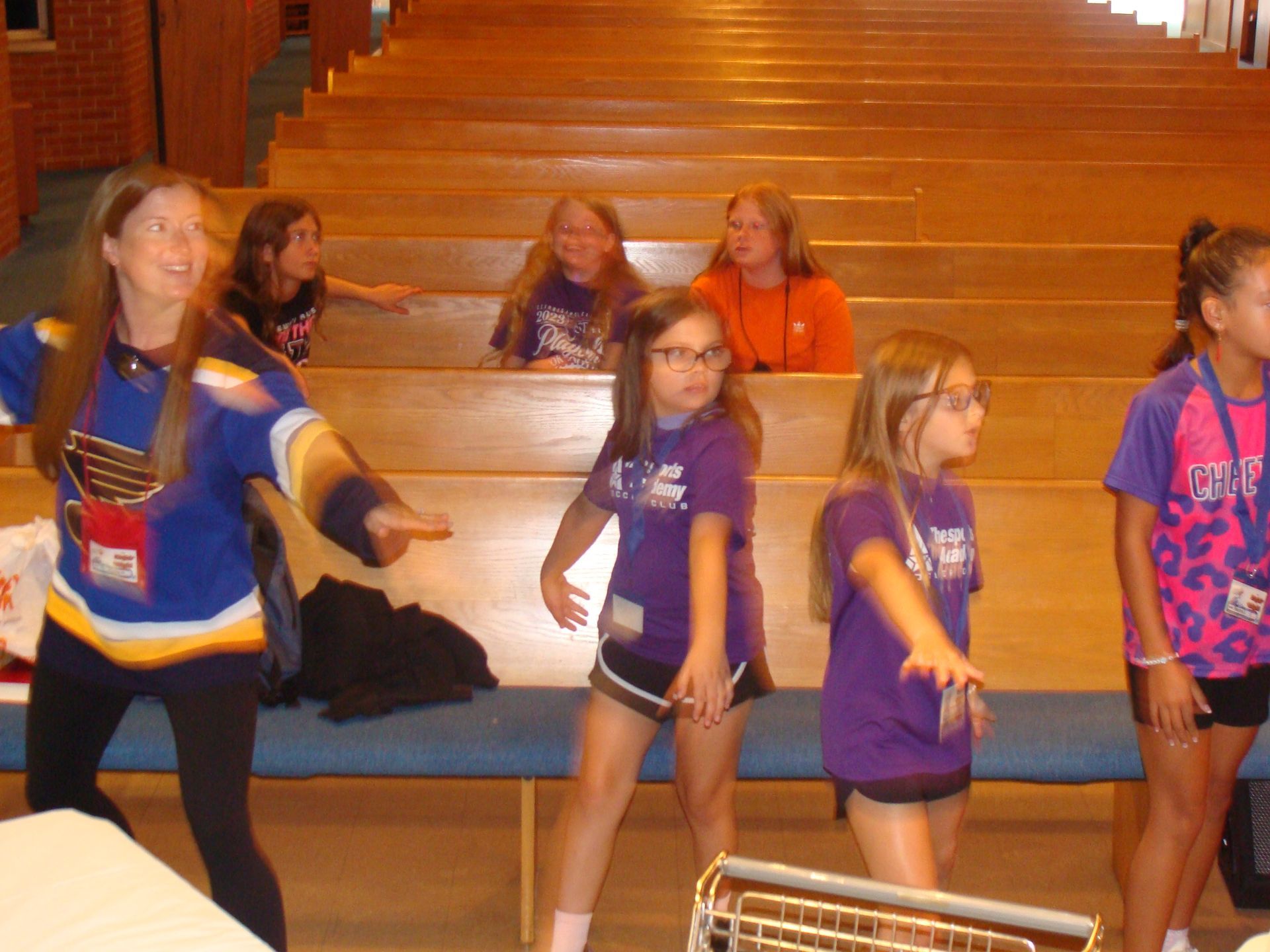 Girls dancing in a gymnasium, with spectators seated on bleachers in the background.