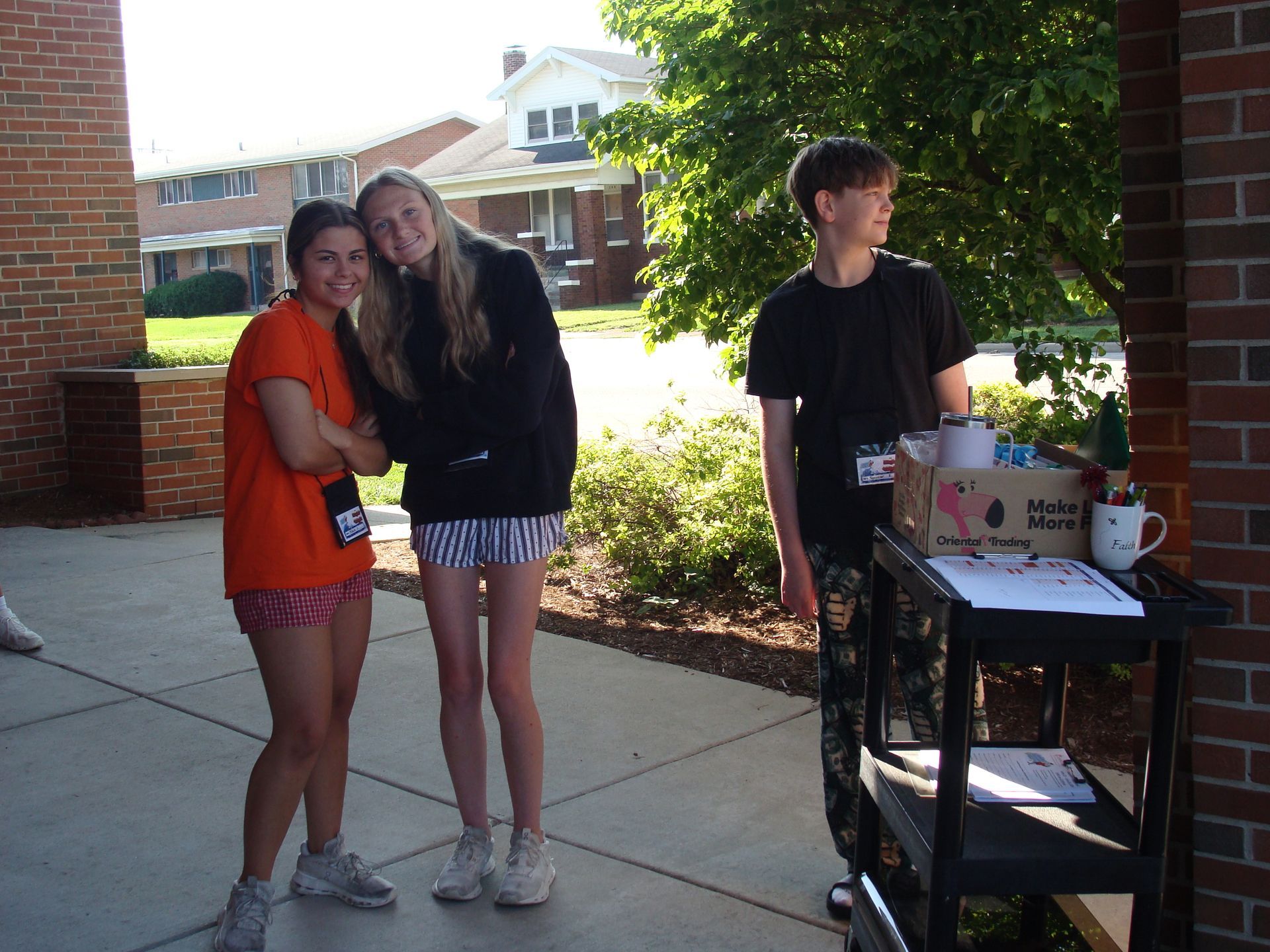 Three people standing on a campus walkway beside a table with boxes and supplies