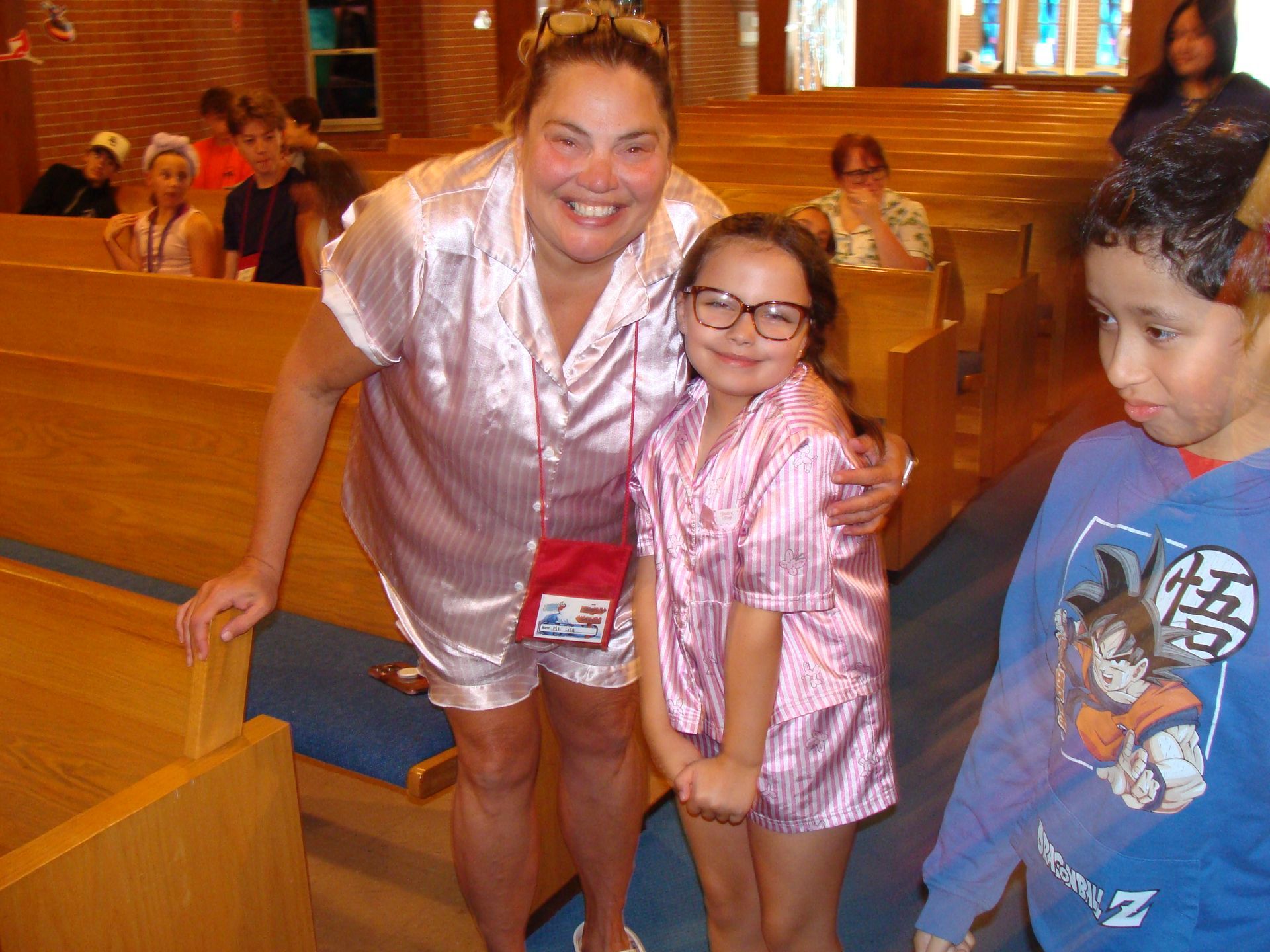Two people in pink shirts smile beside wooden pews in a church or hall.