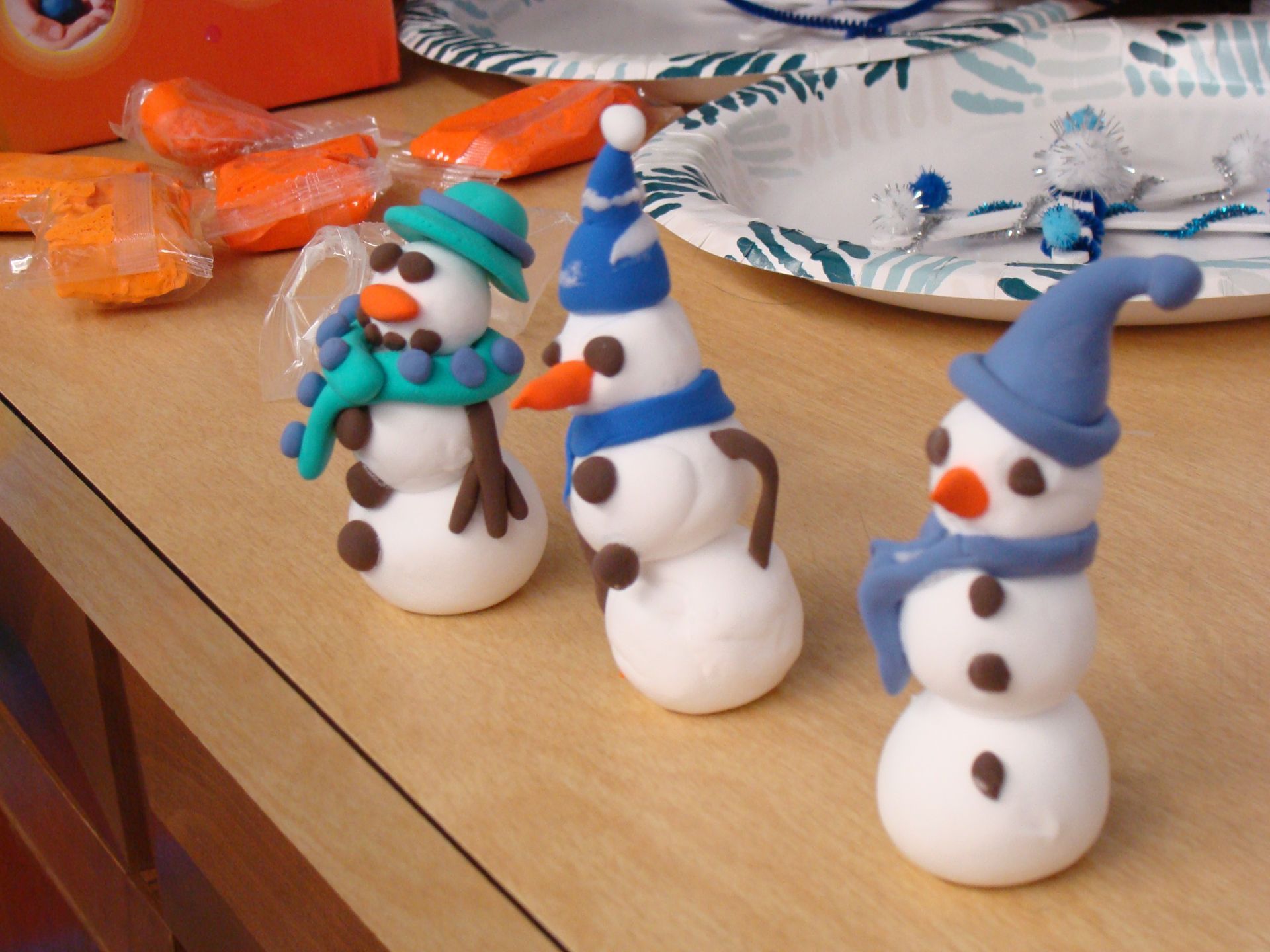 Three small snowman figurines with colorful hats and scarves on a wooden table.