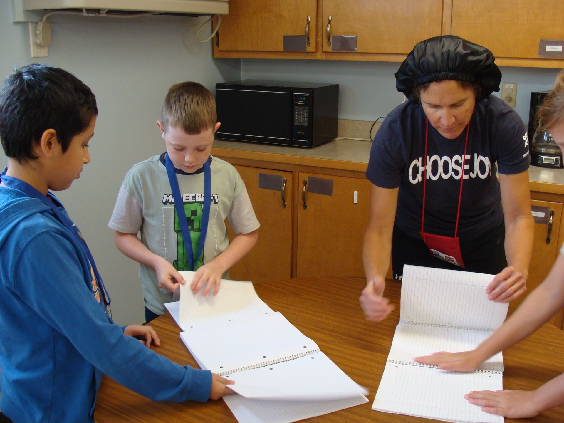Three people reviewing papers together at a kitchen table with cabinets and a microwave in the background