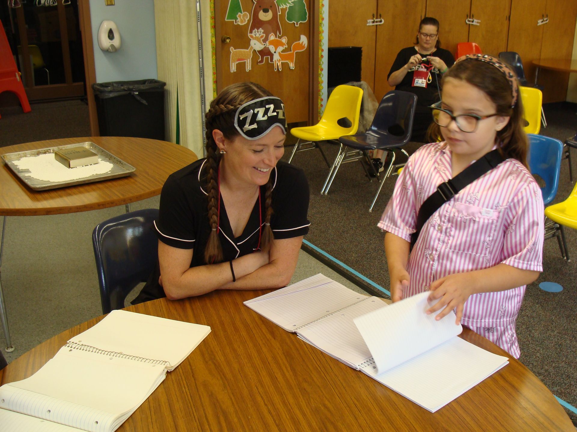 Two women review papers at a table in a classroom or meeting room.
