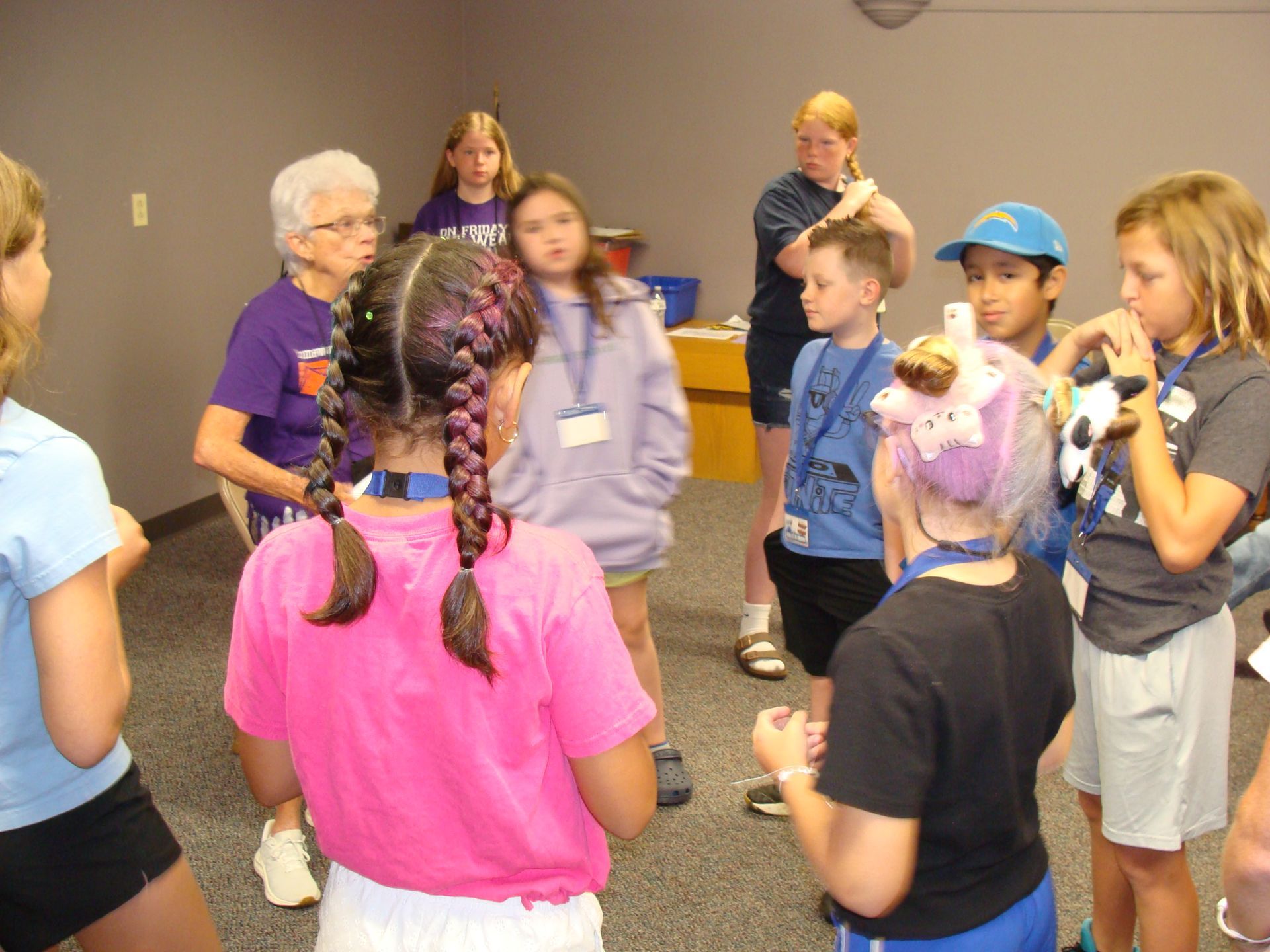 Children stand in a circle listening to an adult in a room with purple walls.