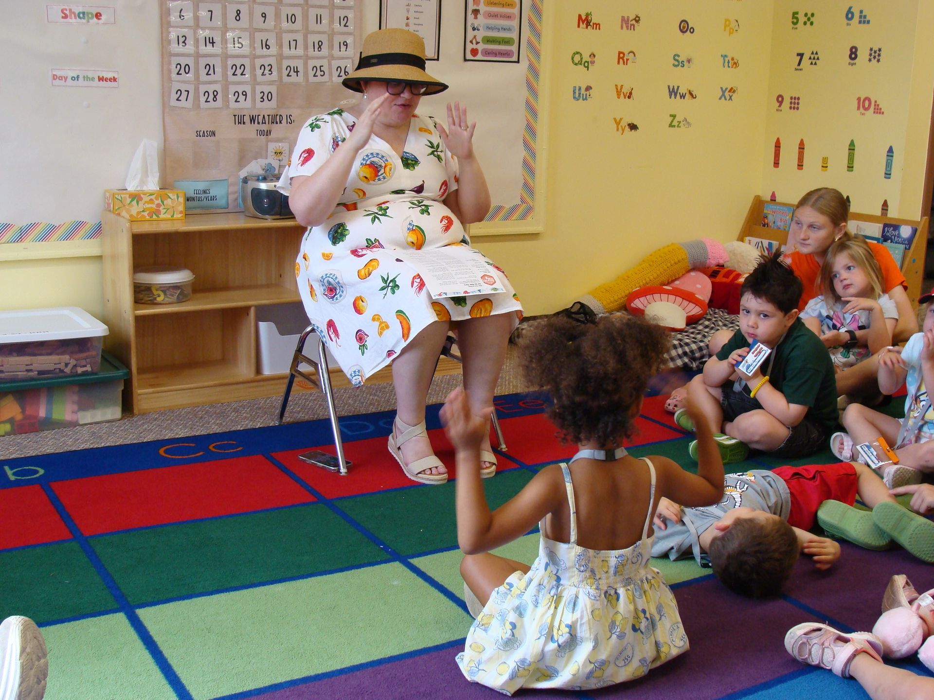 Teacher reading to seated children in a colorful classroom on a red-and-green rug
