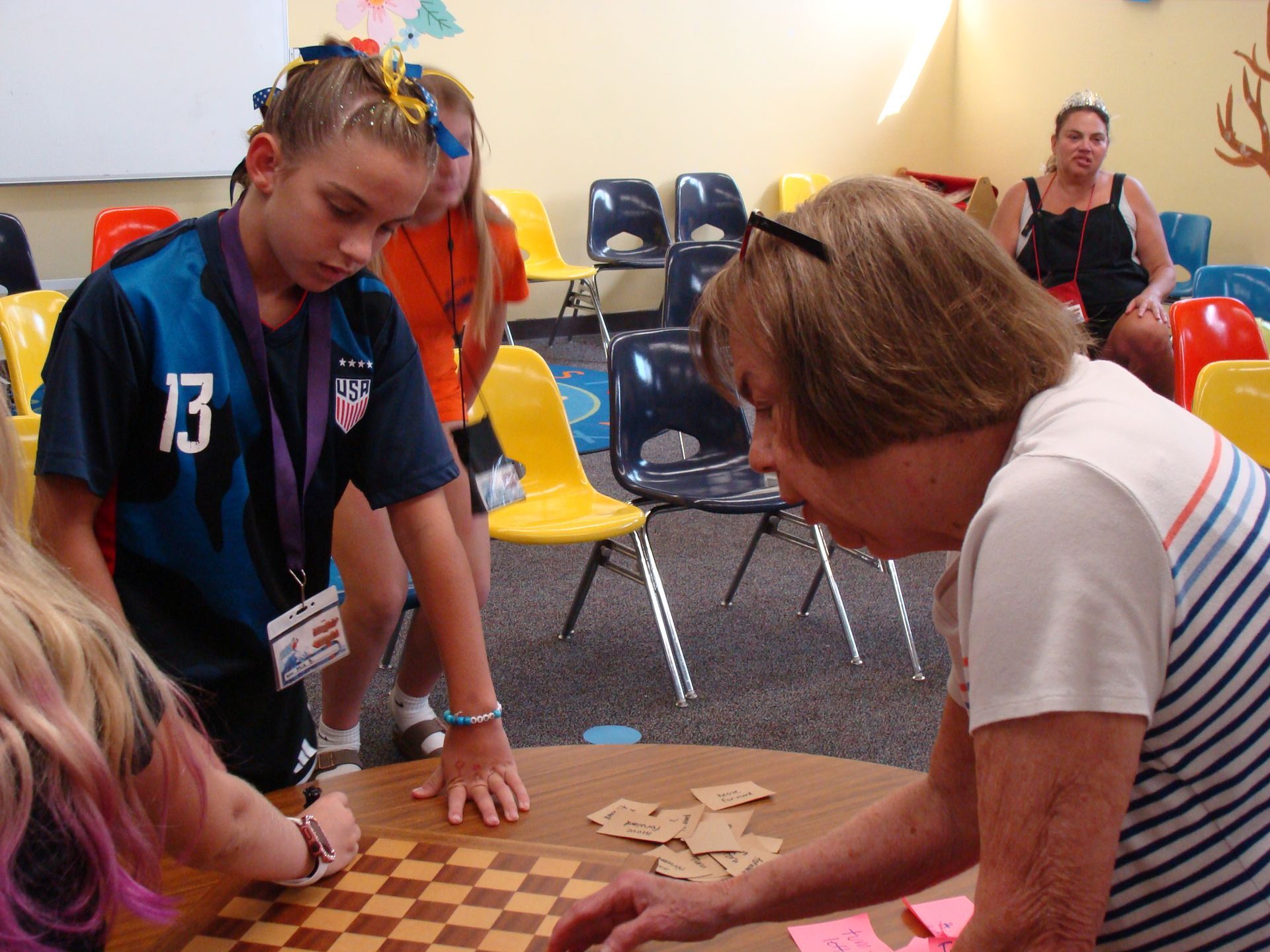 People playing a card game at a table in a room with colorful chairs