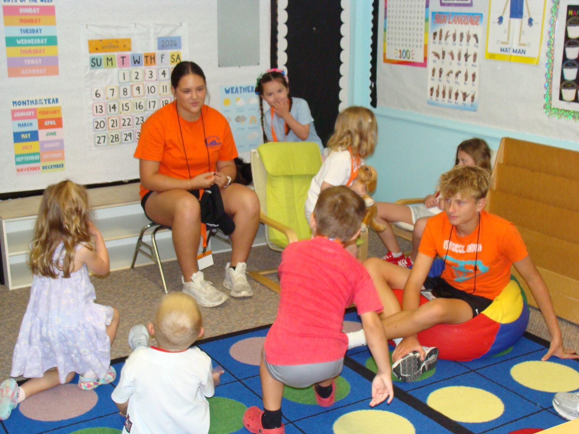 Teacher and children sitting in a colorful classroom circle on a patterned rug