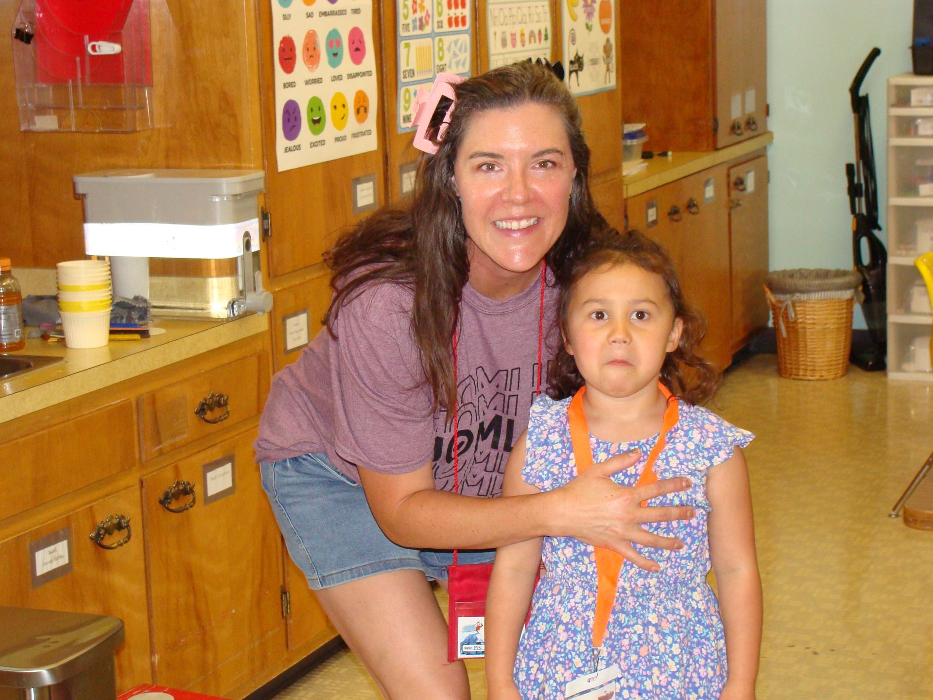 Adult and child posing in a classroom beside wooden cabinets, both looking at the camera.