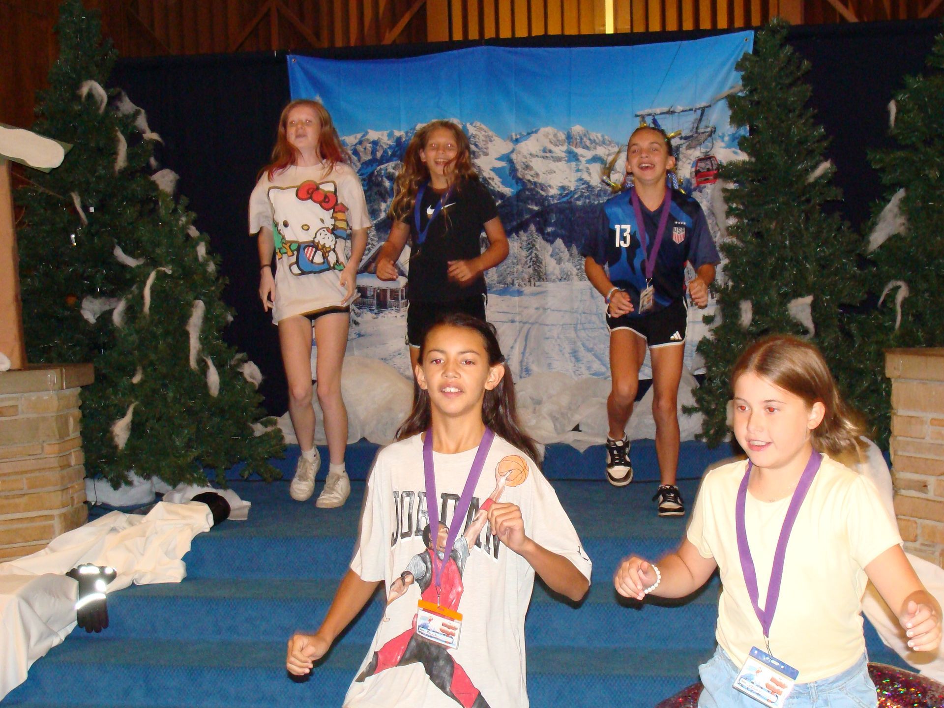 Children running hand-in-hand on a blue stage with a snowy winter backdrop and decorations