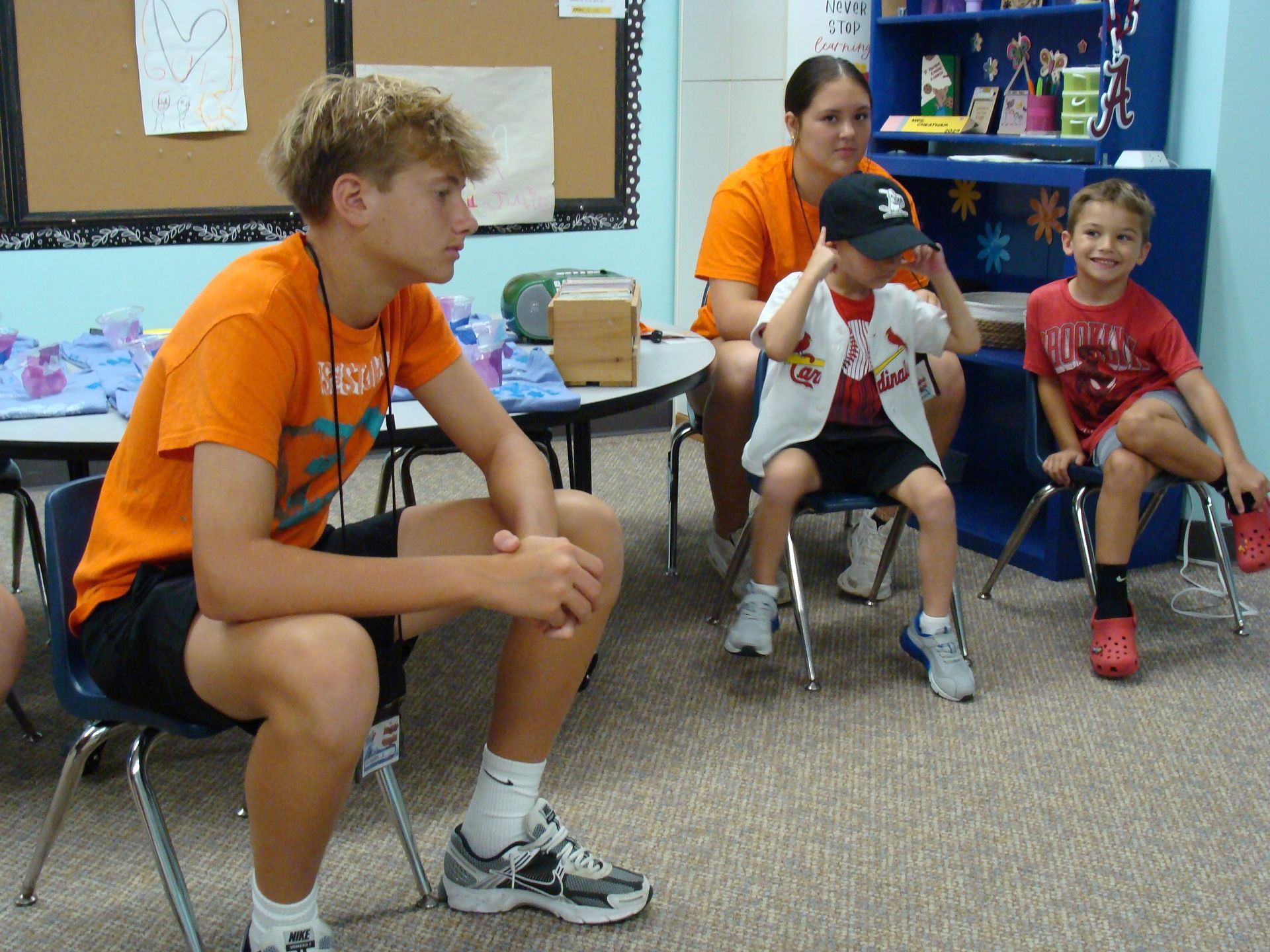 People sitting on chairs in a classroom, including one person in an orange shirt leaning forward.
