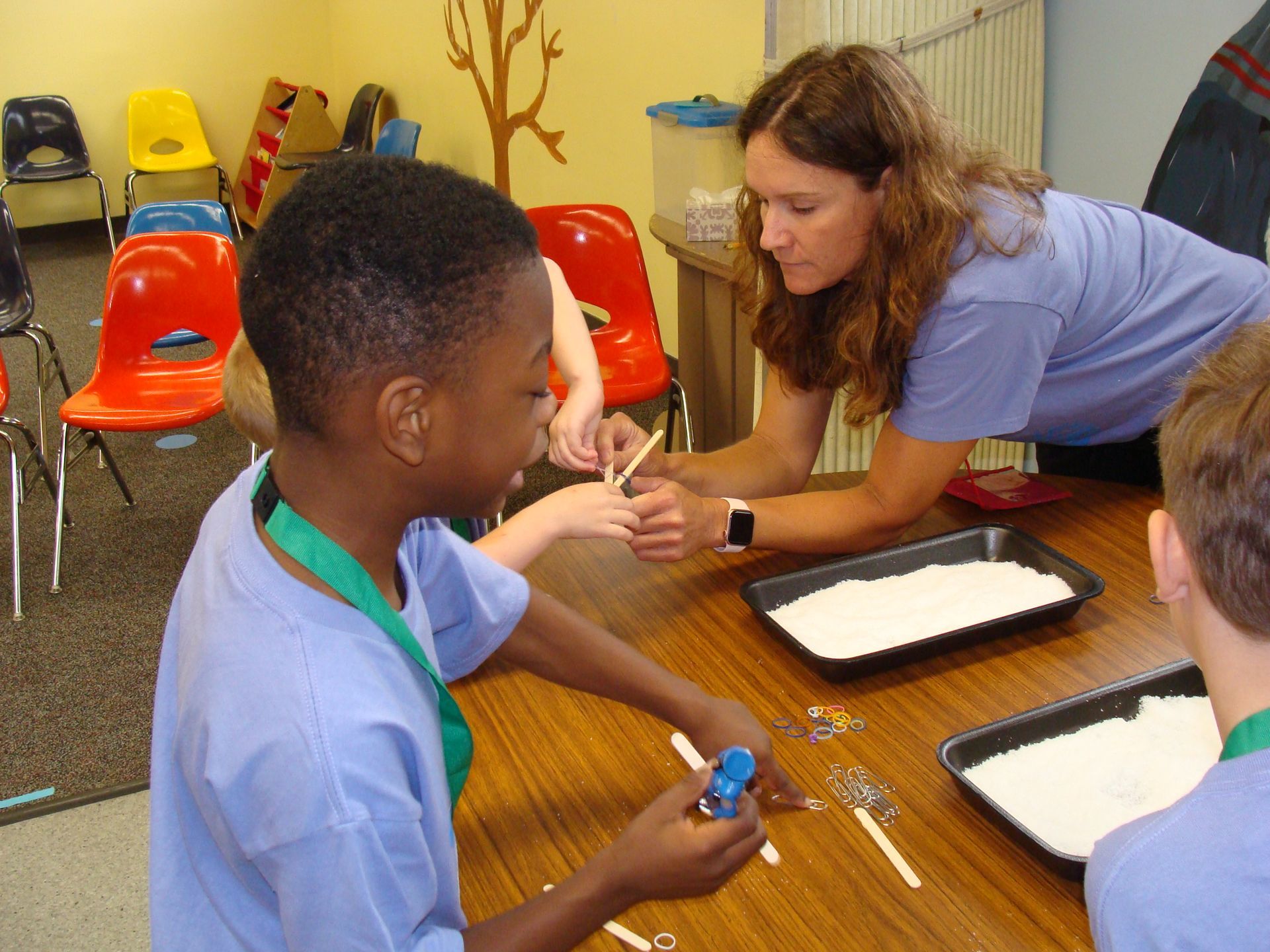 Teacher helping children with a classroom activity at a table with trays and craft materials