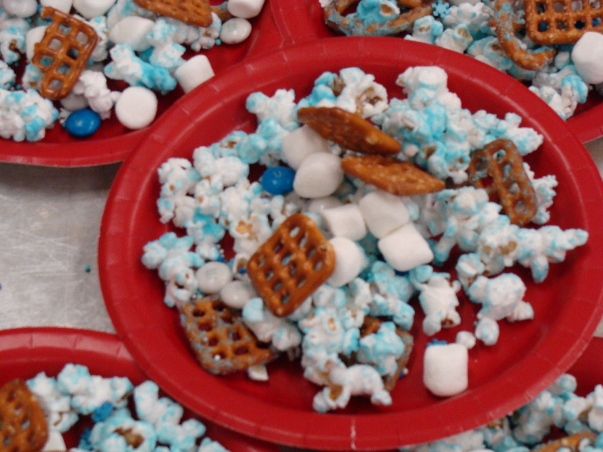 Red plate piled with blue popcorn, marshmallows, and waffle pieces on a table