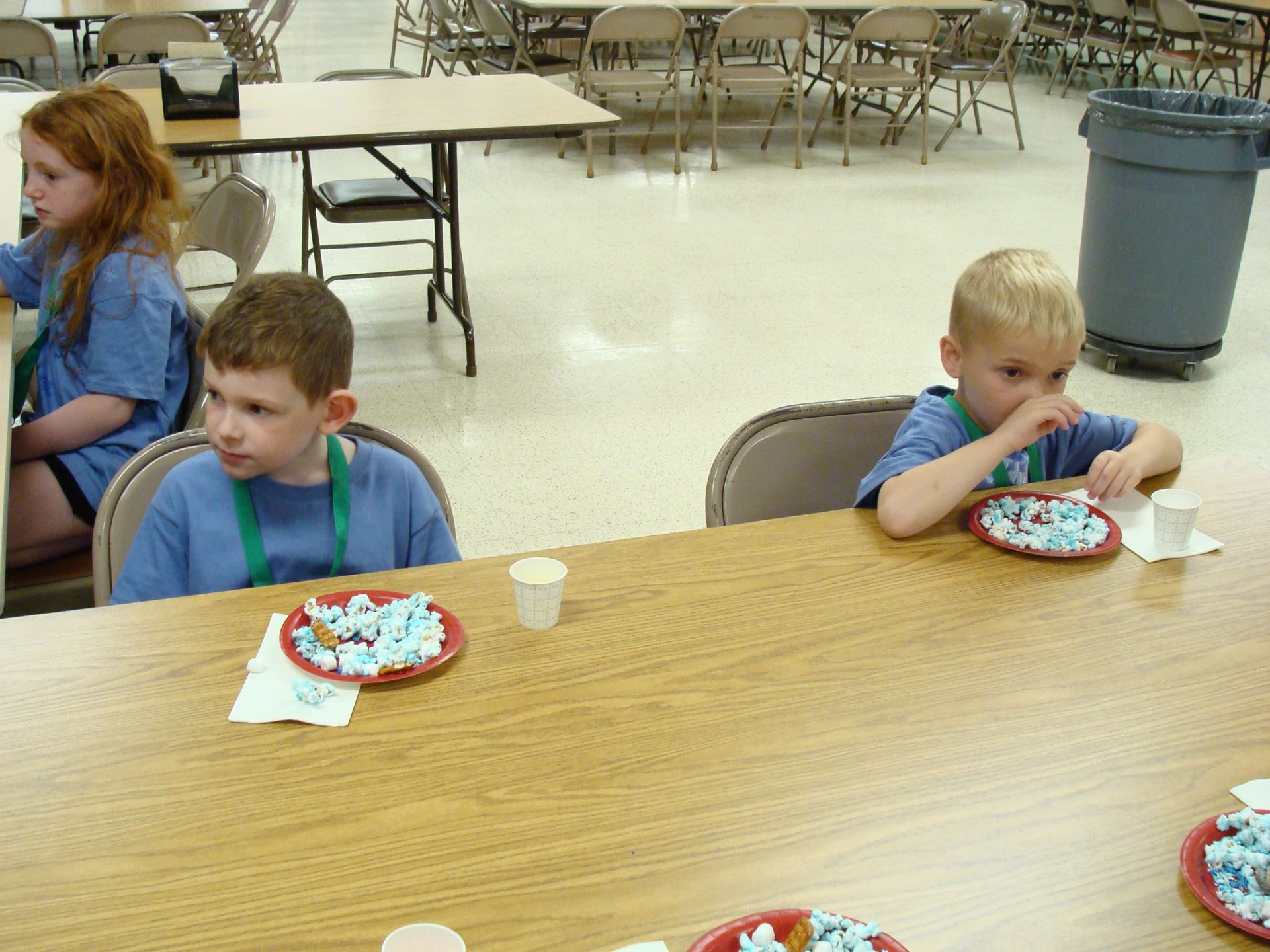 Children eating dessert at a table in a cafeteria with empty tables and chairs in the background