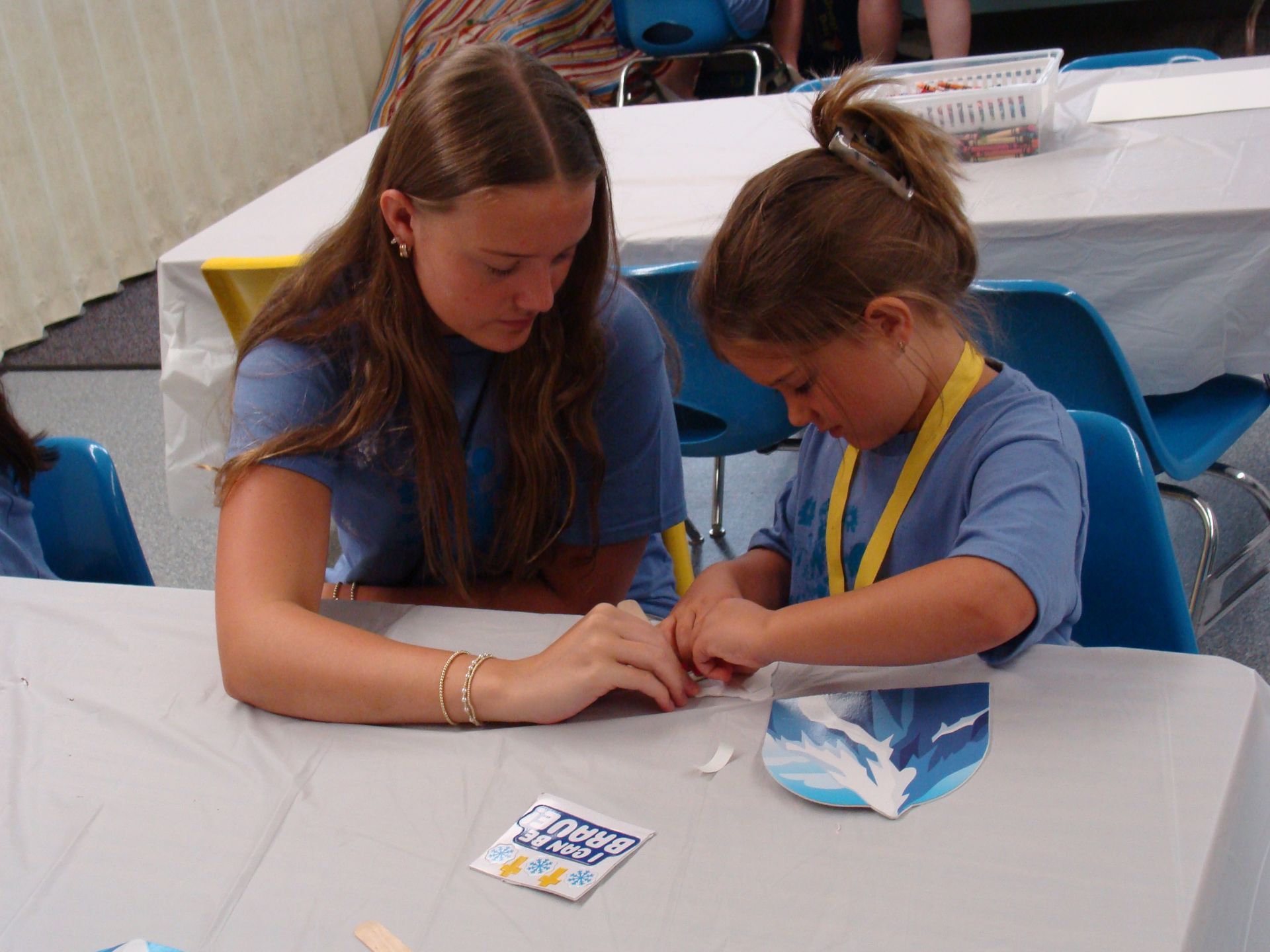 Two children at a table making a craft together, focused on a small activity in a bright room