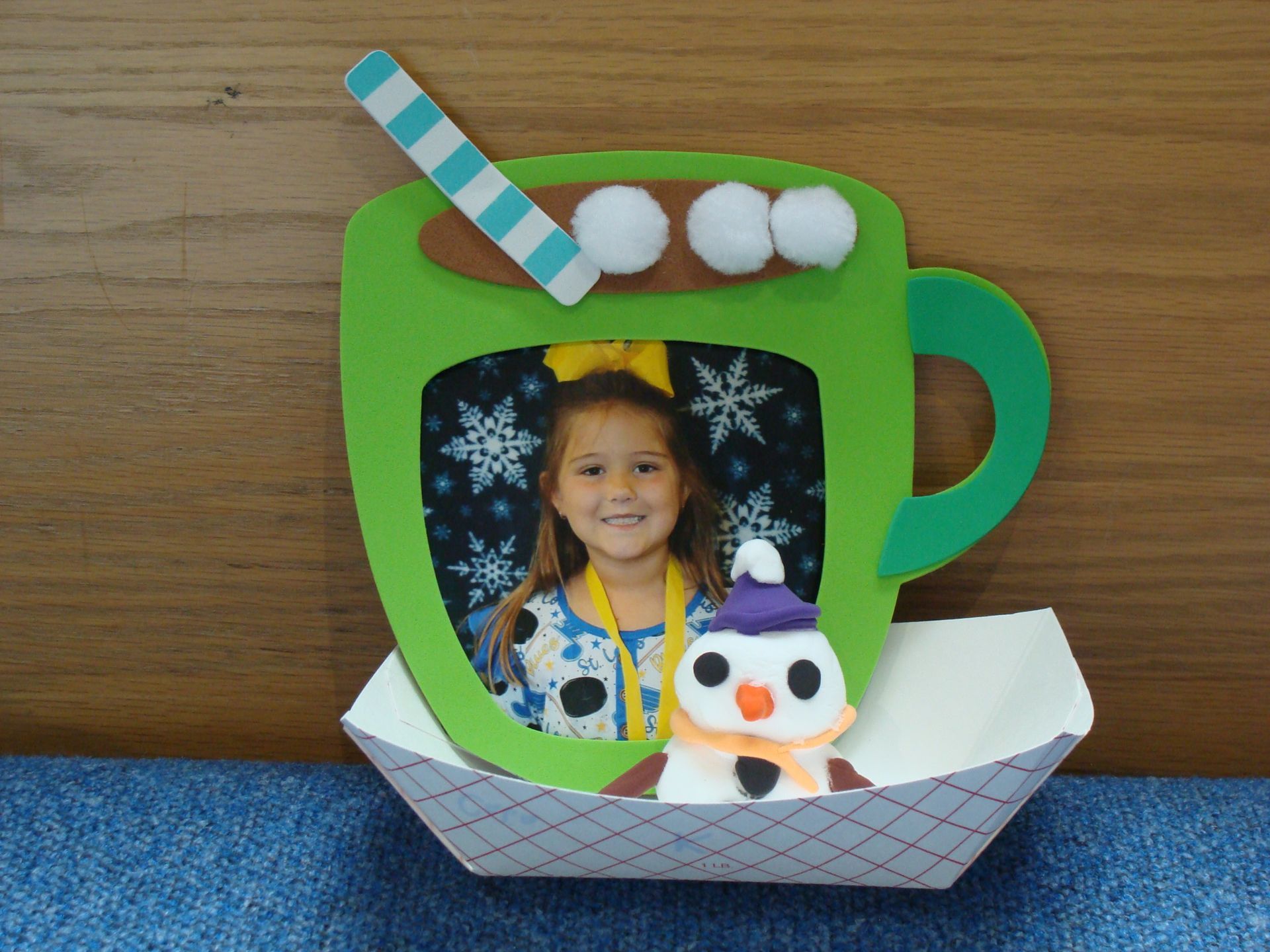 Green mug-shaped craft with a child’s photo, striped straw, cotton “steam,” and a small snowman on a paper base