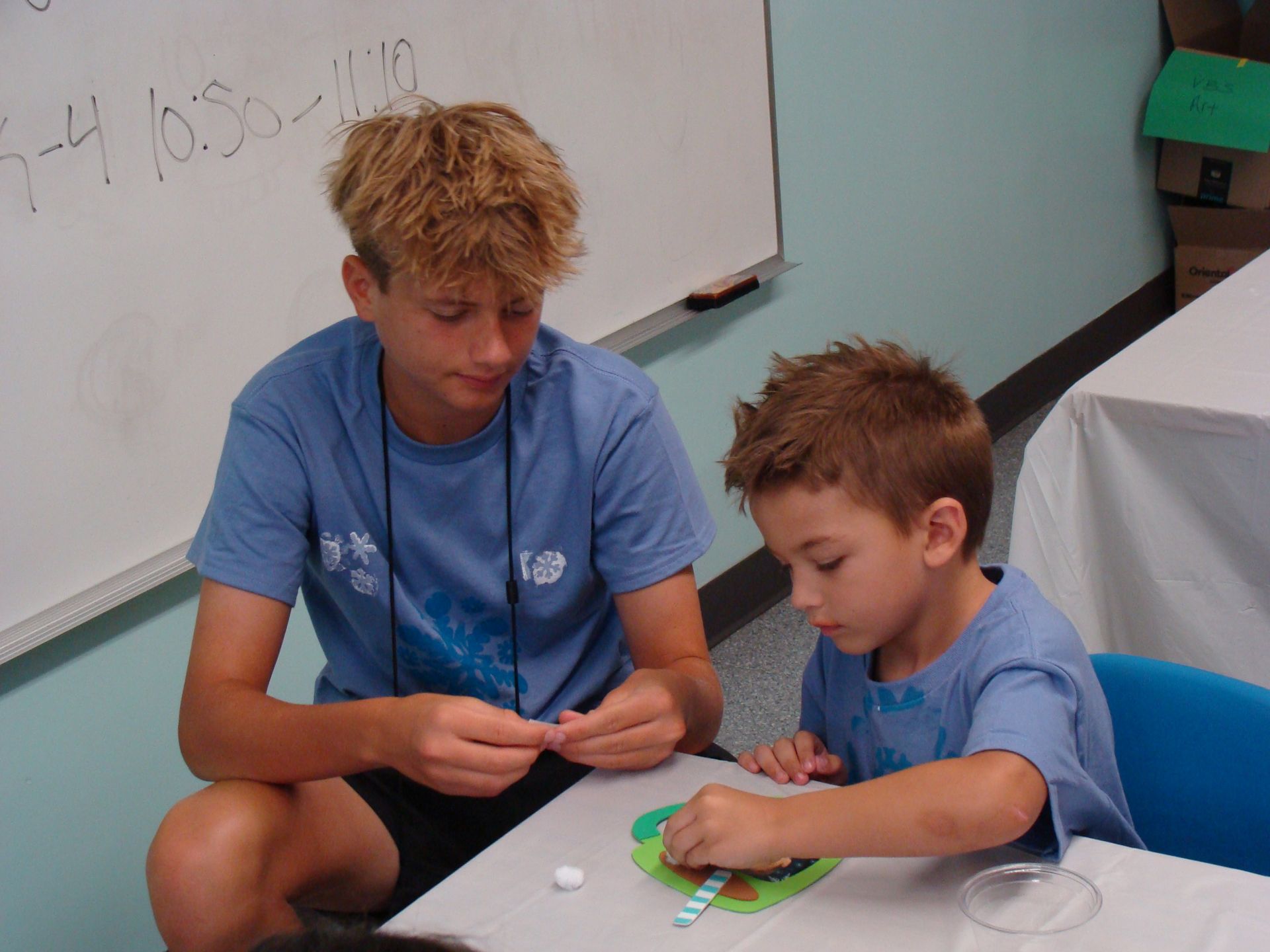 Two people in blue shirts playing a tabletop activity beside a whiteboard