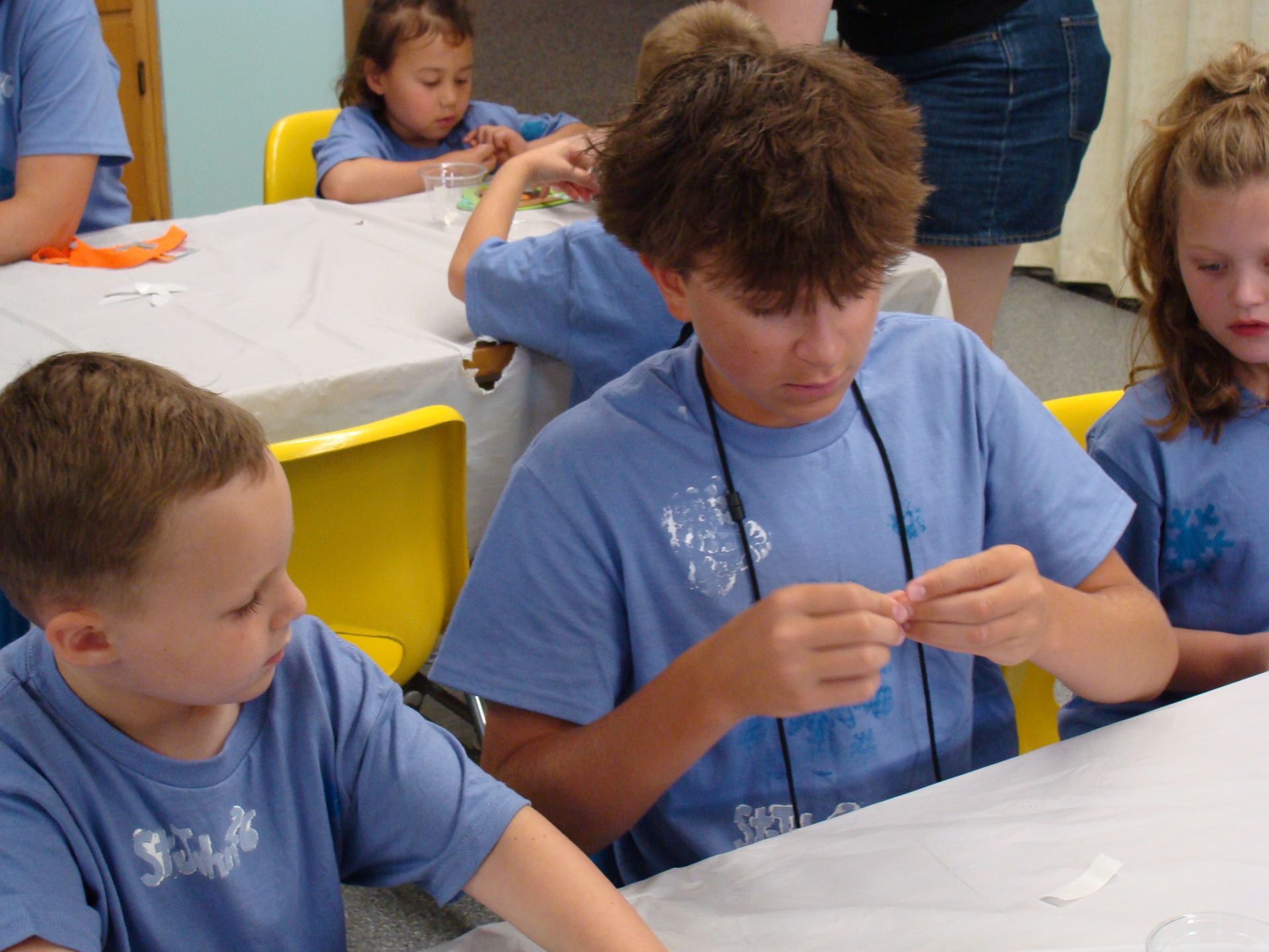 Children in blue shirts making crafts at a table in a classroom