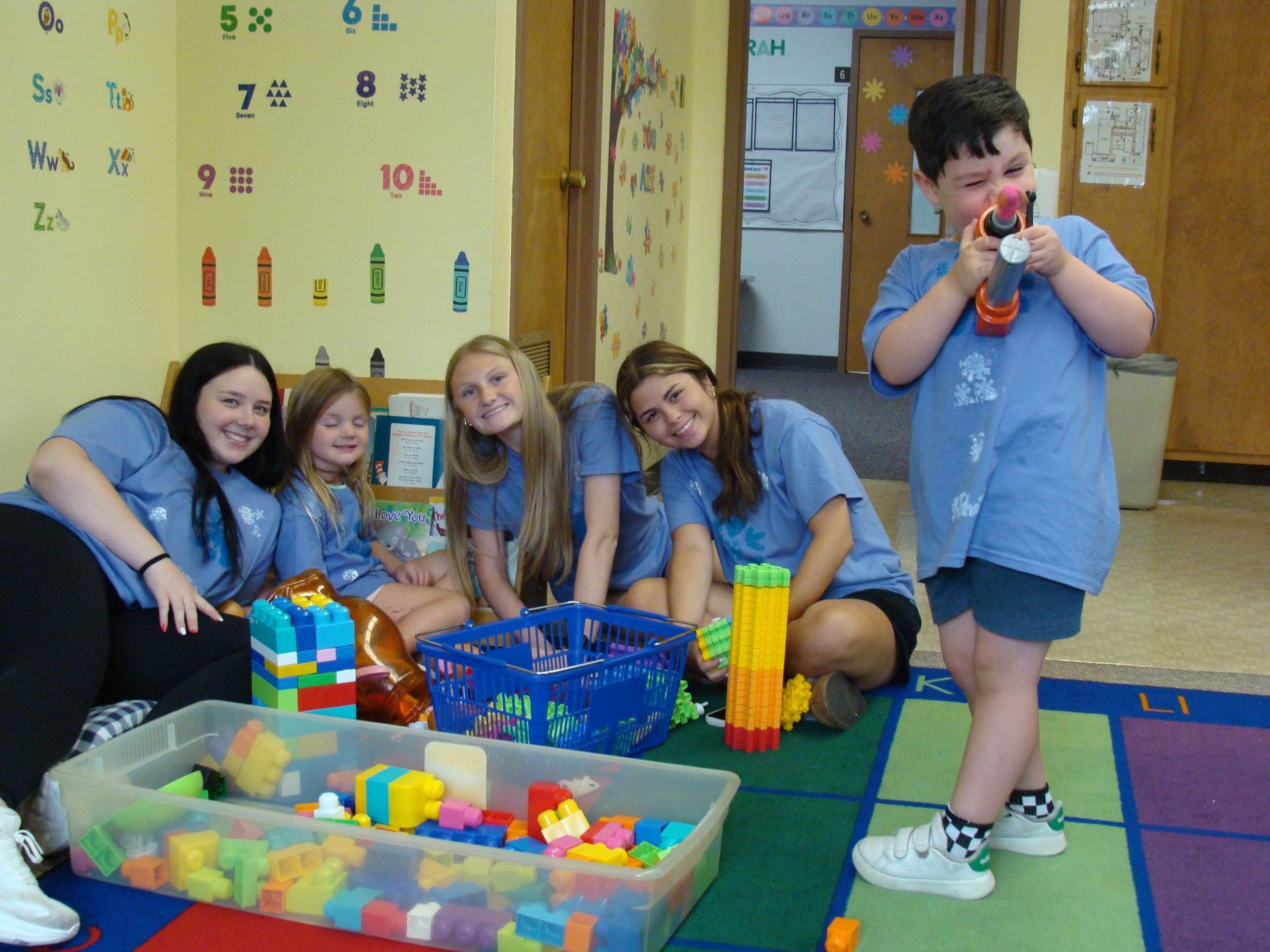 Children in blue shirts playing with colorful blocks on a classroom rug