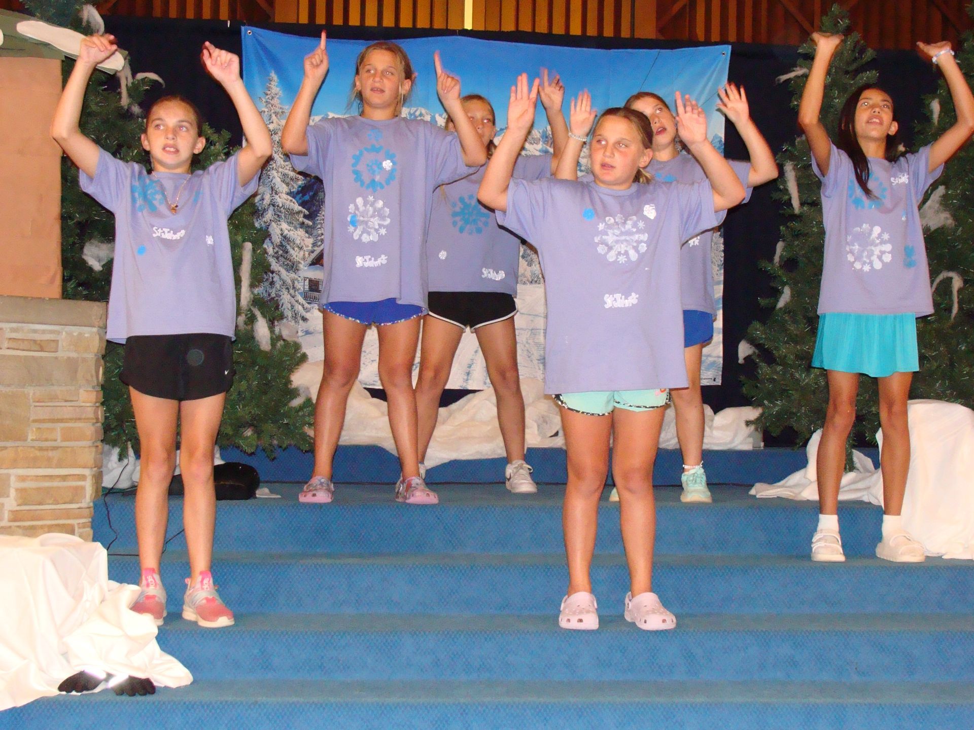Five people on blue steps with arms raised, wearing matching purple shirts during a group performance