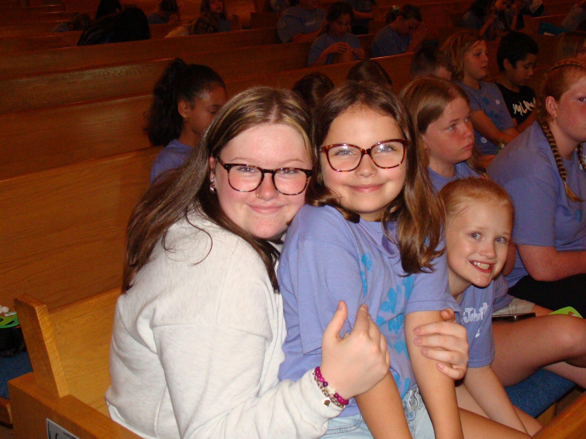 Three smiling children seated in bleachers, giving thumbs up.