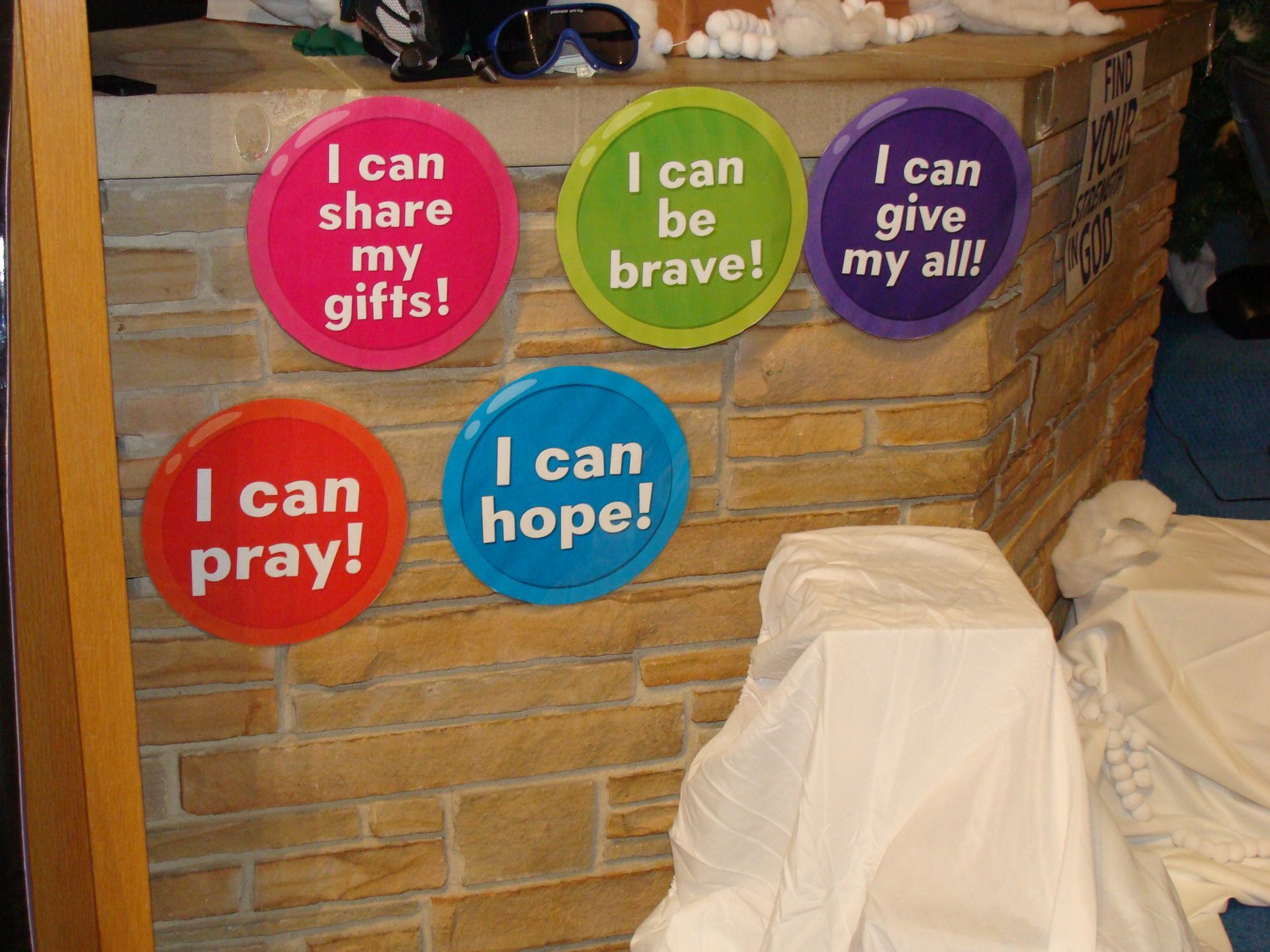 Colorful church posters with faith messages beside a draped chair and woven basket storage.