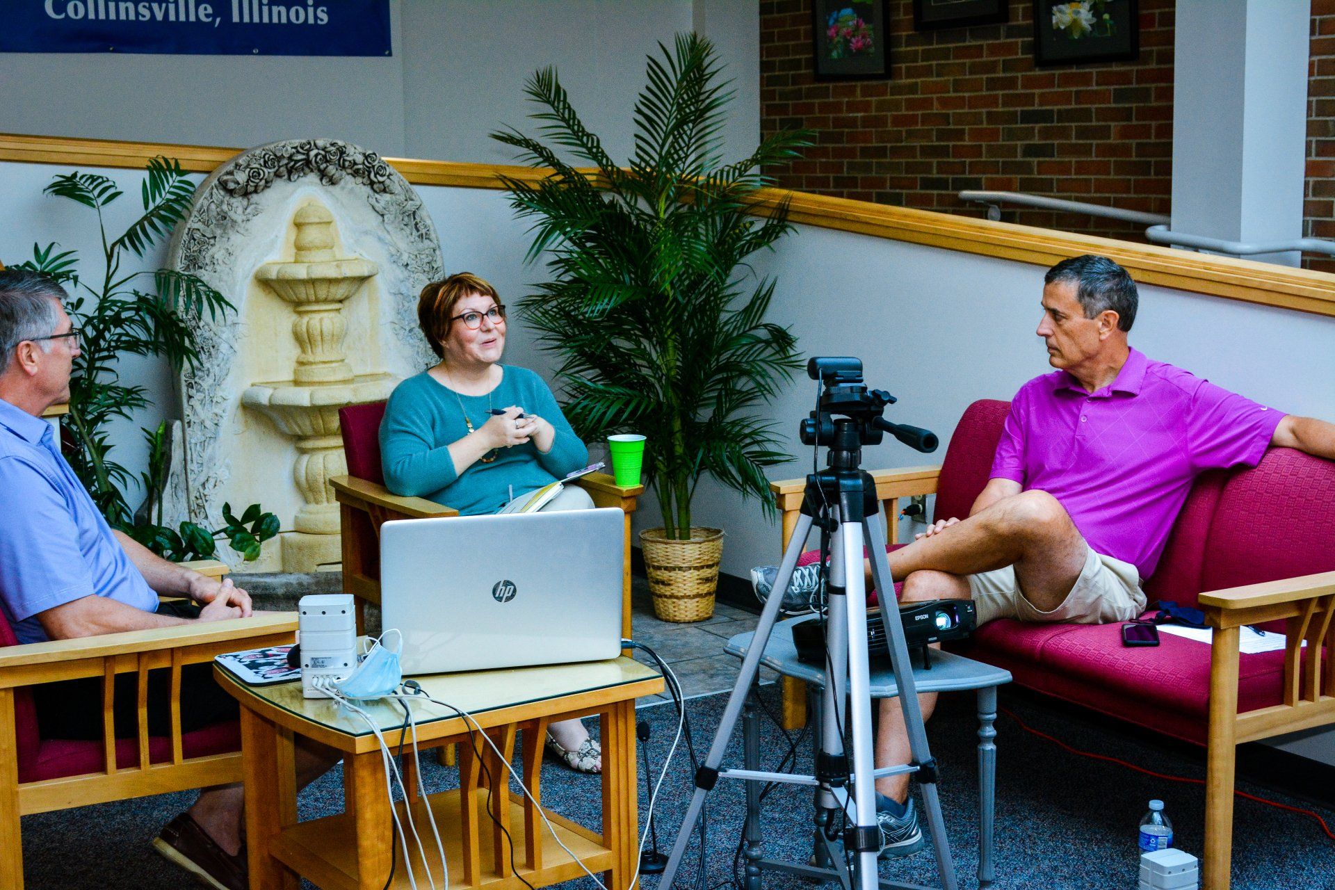Three people in conversation with a laptop and camera tripod in a cozy indoor studio set