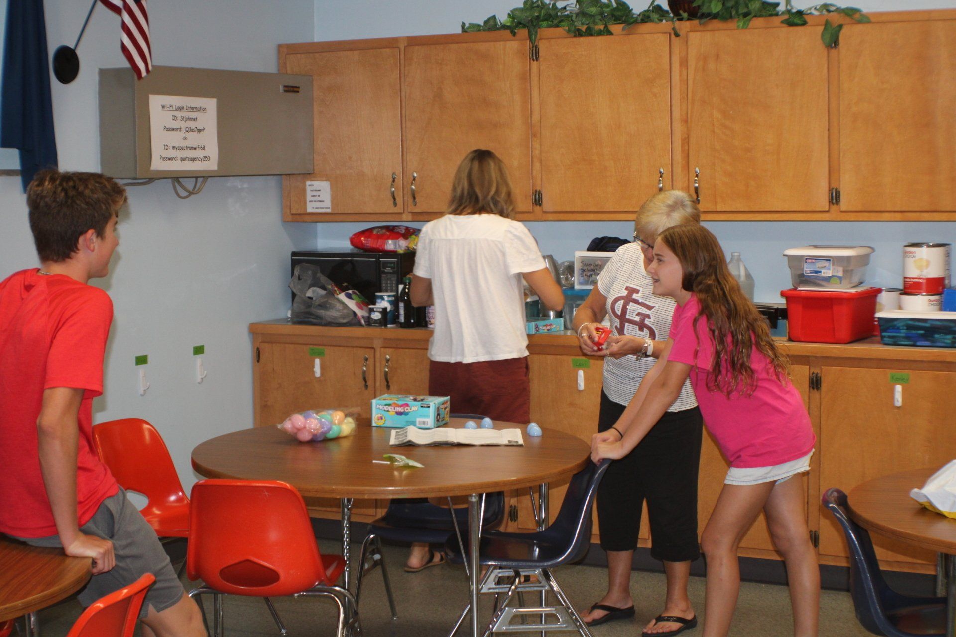 Children gathered around a table in a classroom kitchen, reaching for items on the counter.