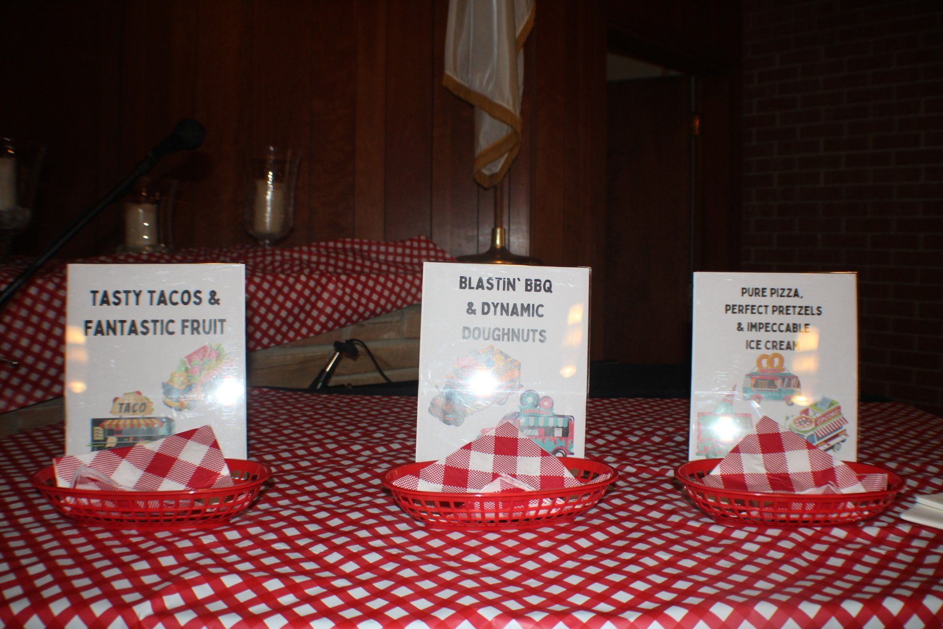 Three table signs on red cloth display tasting notes for tacos, brisket, and pork at an event.