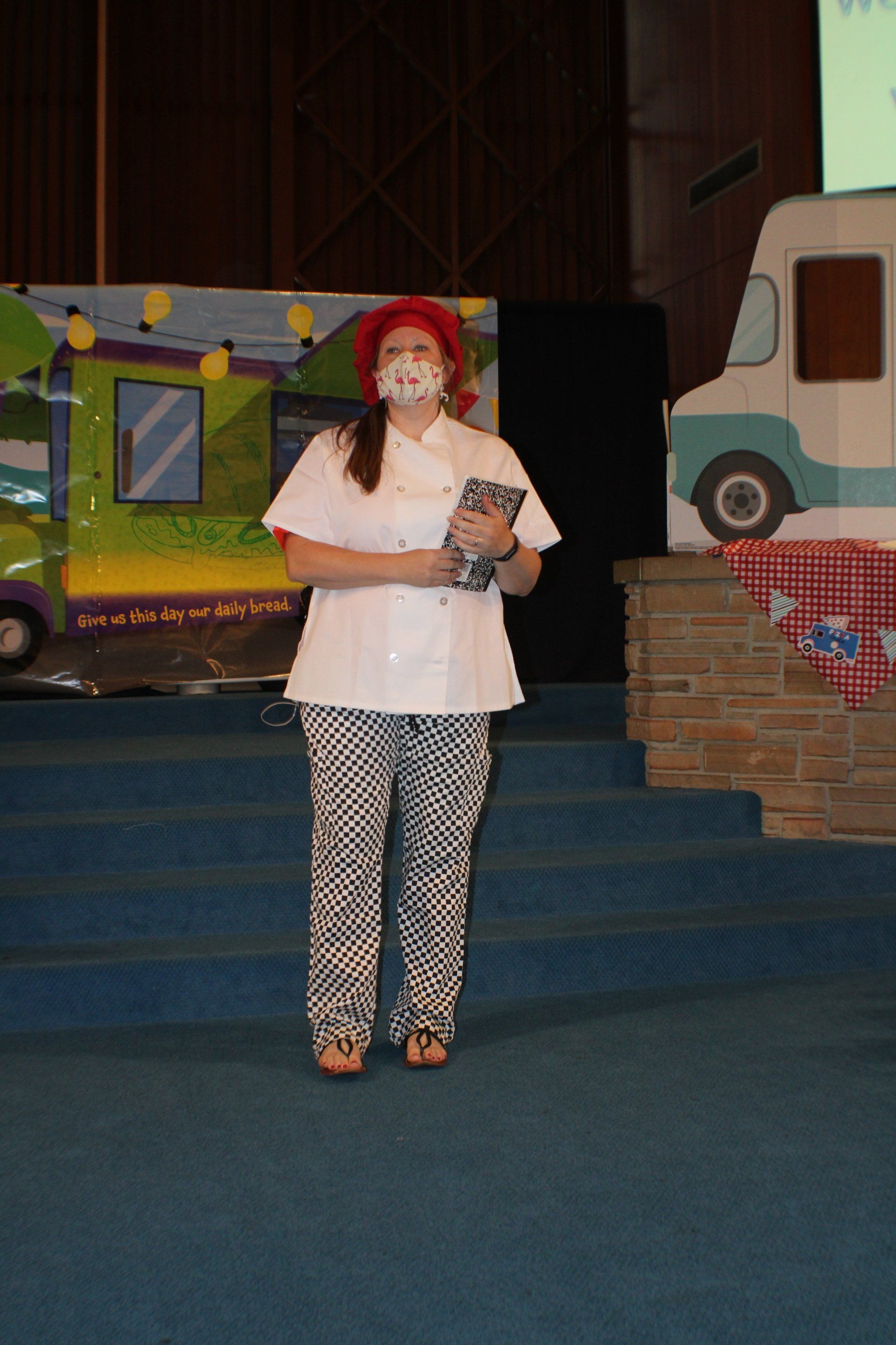 Person in white shirt and patterned pants holding a doll on a stage with colorful backdrops and steps