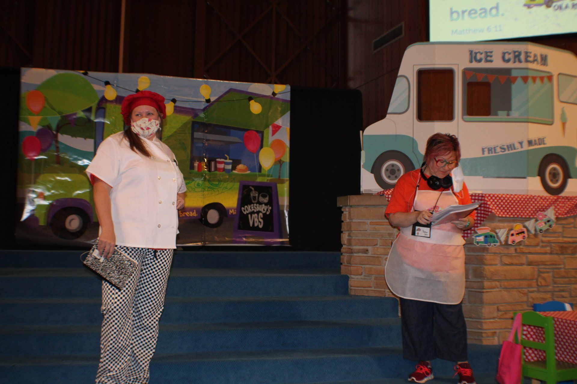 Two people on a stage beside a colorful ice cream truck backdrop