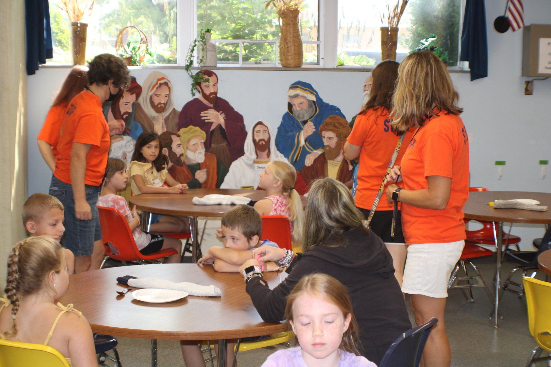 People in orange shirts serving food at tables in a community dining room