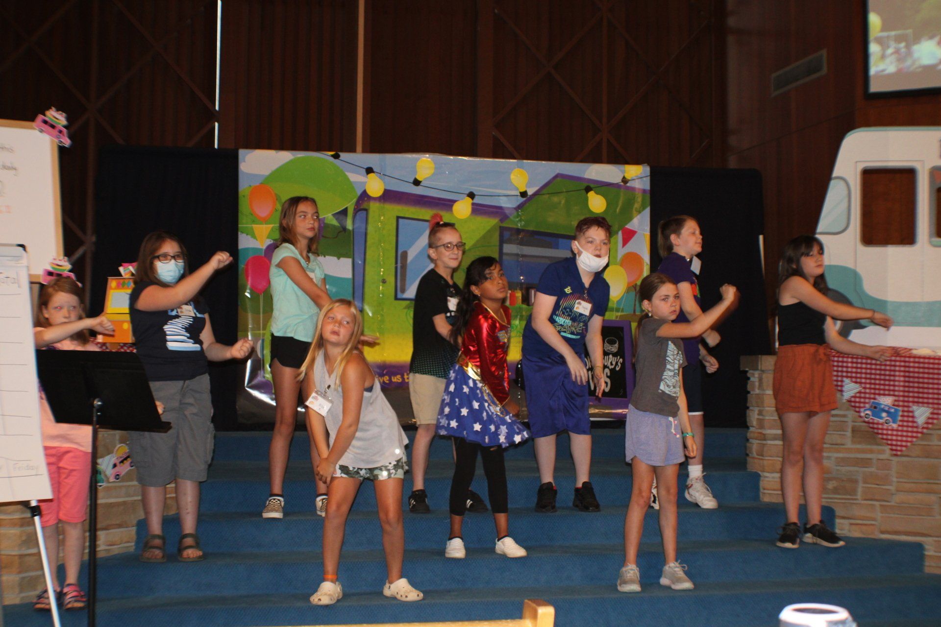 Children dancing on a school stage in front of a colorful backdrop