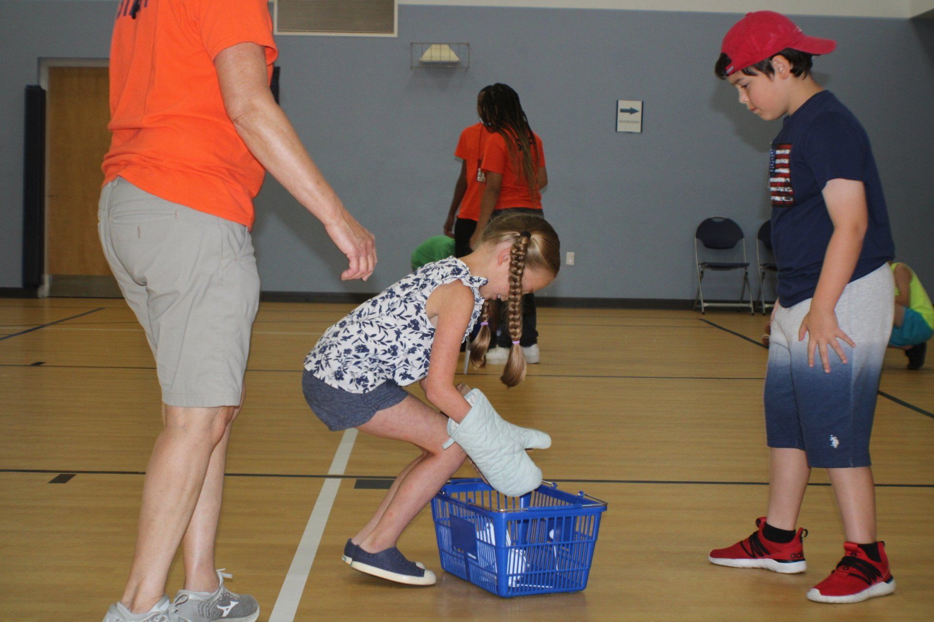 Children playing a beanbag game in a gym, with one child crouched over a blue crate.
