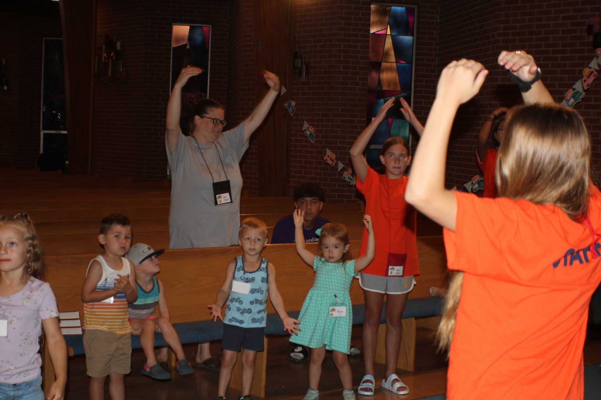 Children in a classroom stretch with an instructor in an orange shirt leading them