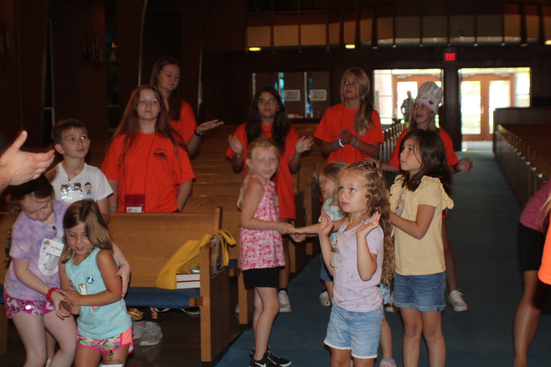 Children in bright shirts standing and sitting in a hallway, some posing with hands raised