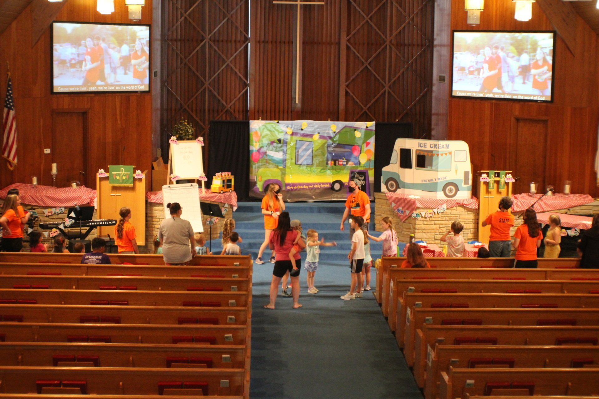 Children and adults in a church hall with colorful displays and toy vehicles, seen from the pews.