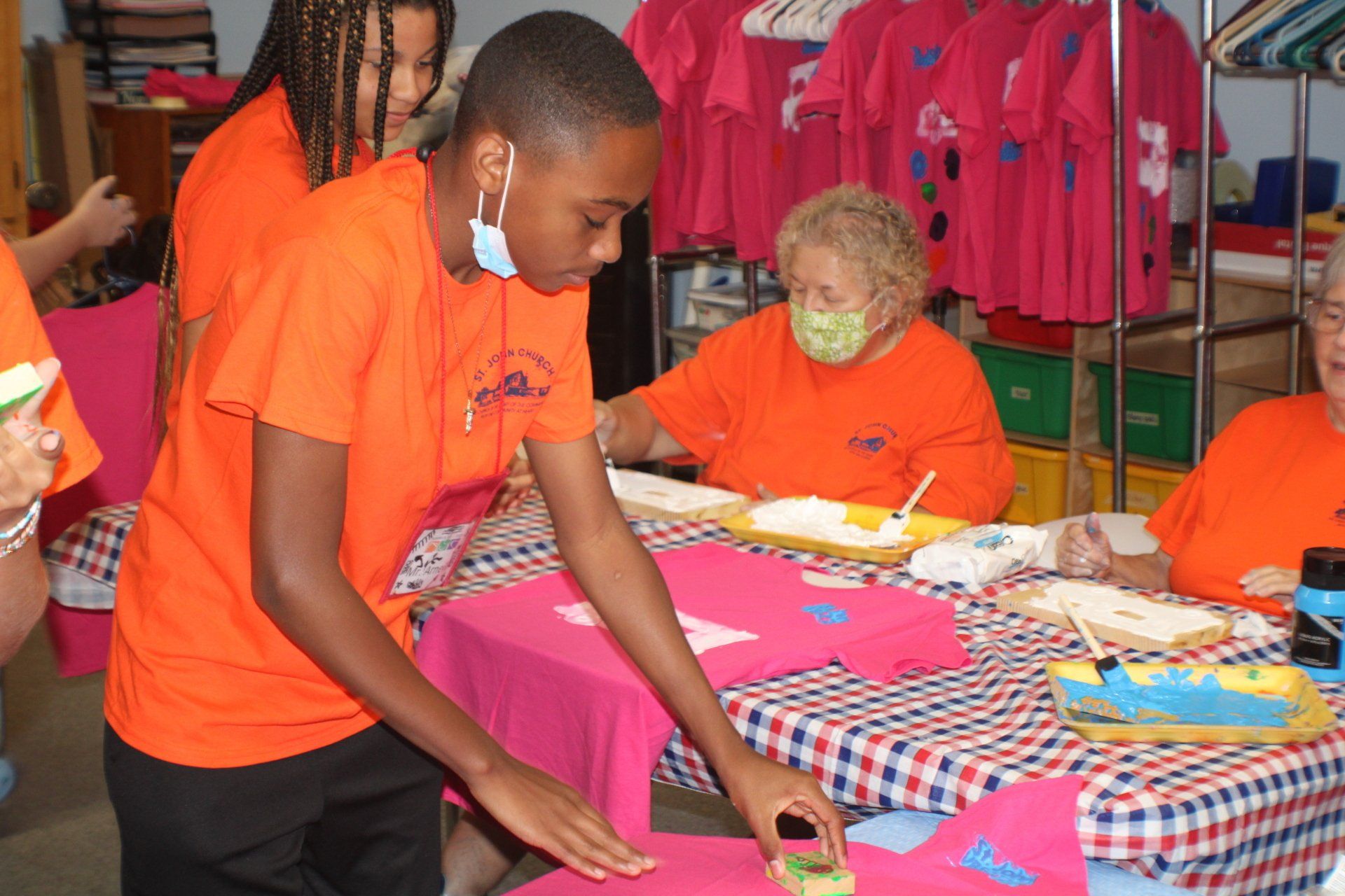 People in orange shirts folding fabric at a table in a colorful craft booth