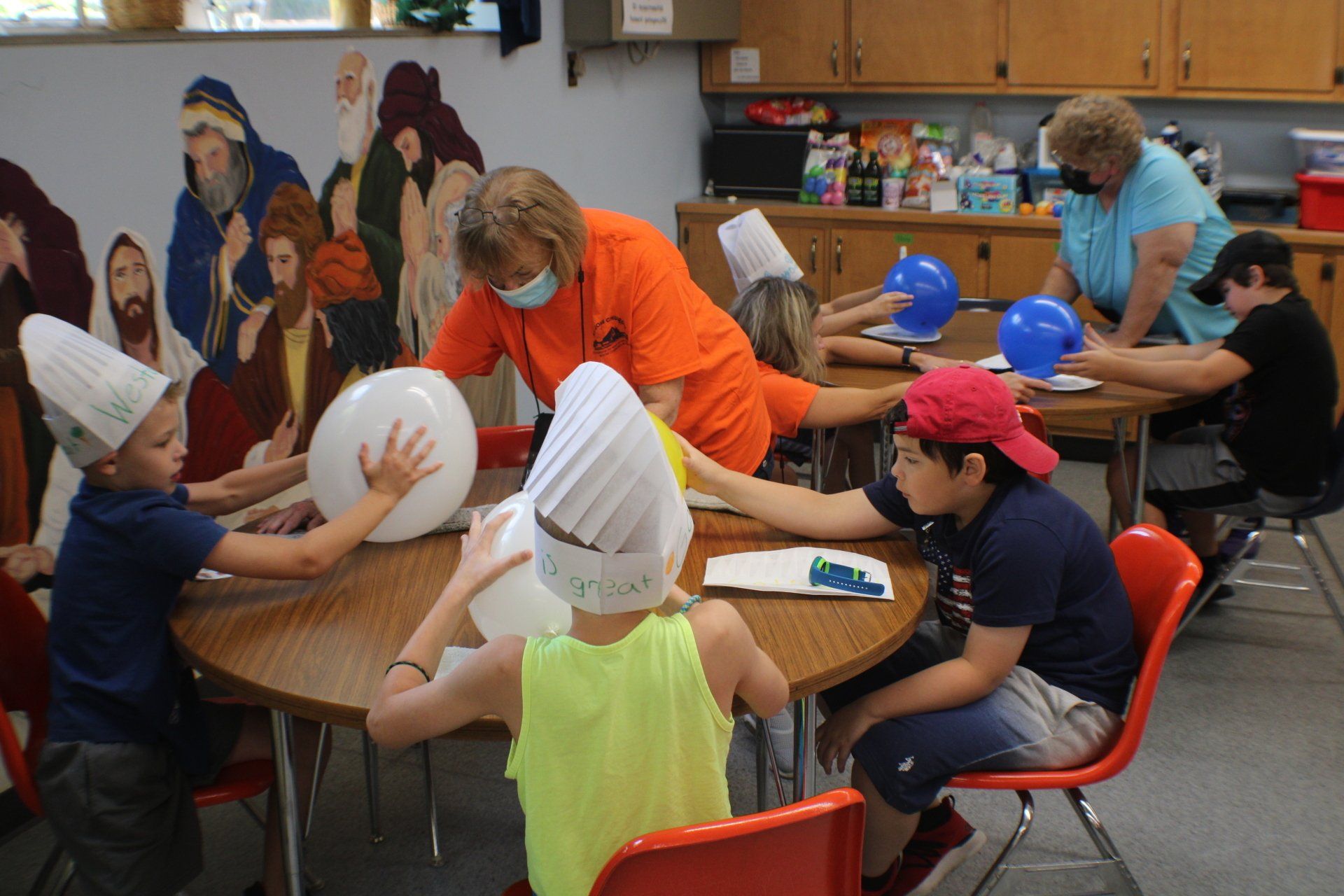 Children in chef hats decorate round tables in a classroom art activity