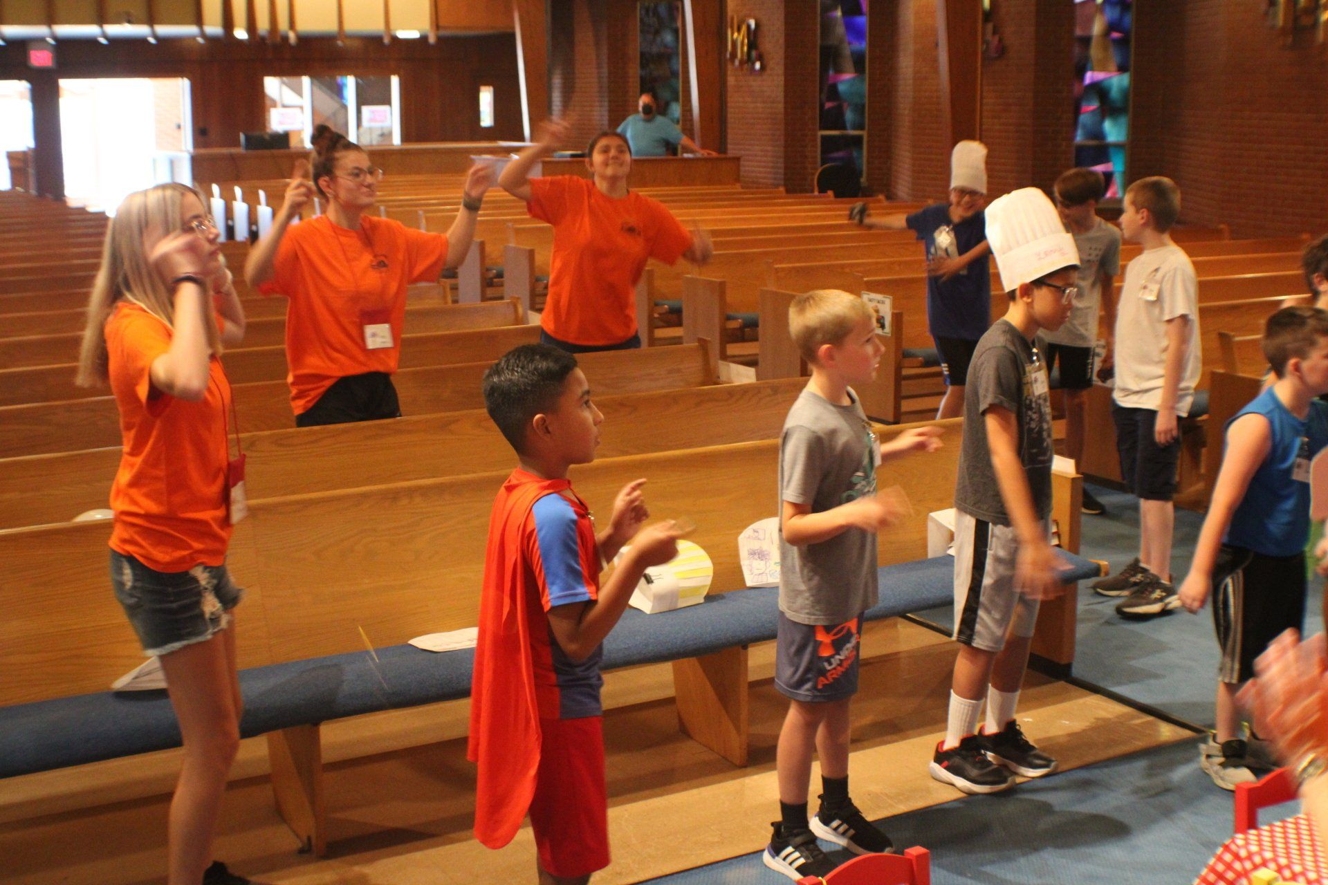 Children in orange shirts practice balance exercises in a gym with wooden benches