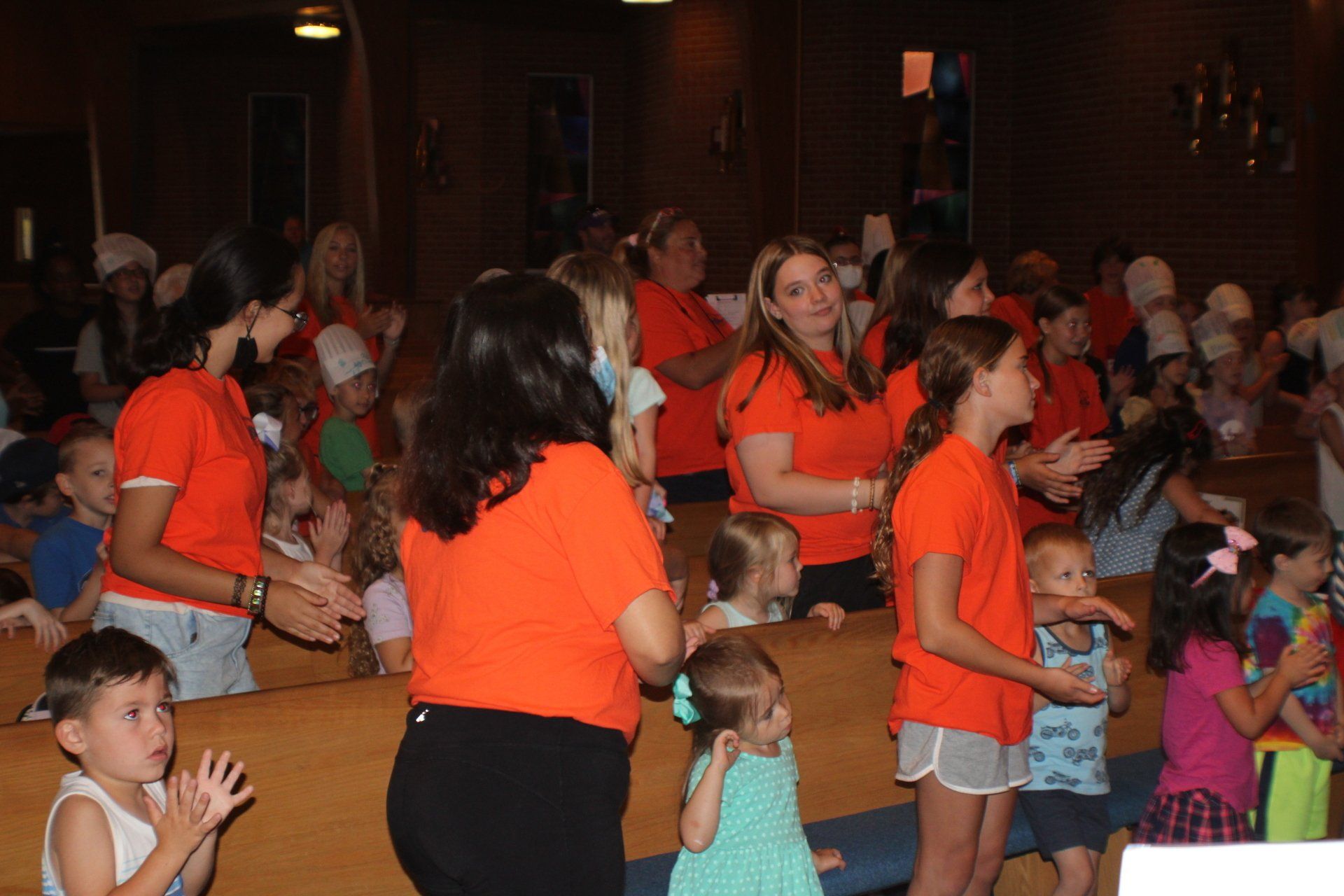 Crowd of people in orange shirts singing and dancing in a dim indoor hall