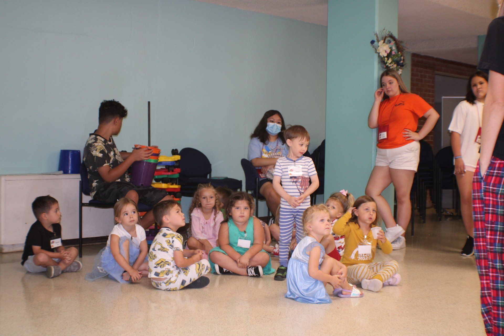 Children sitting on the floor in a dance studio, watching adults nearby.