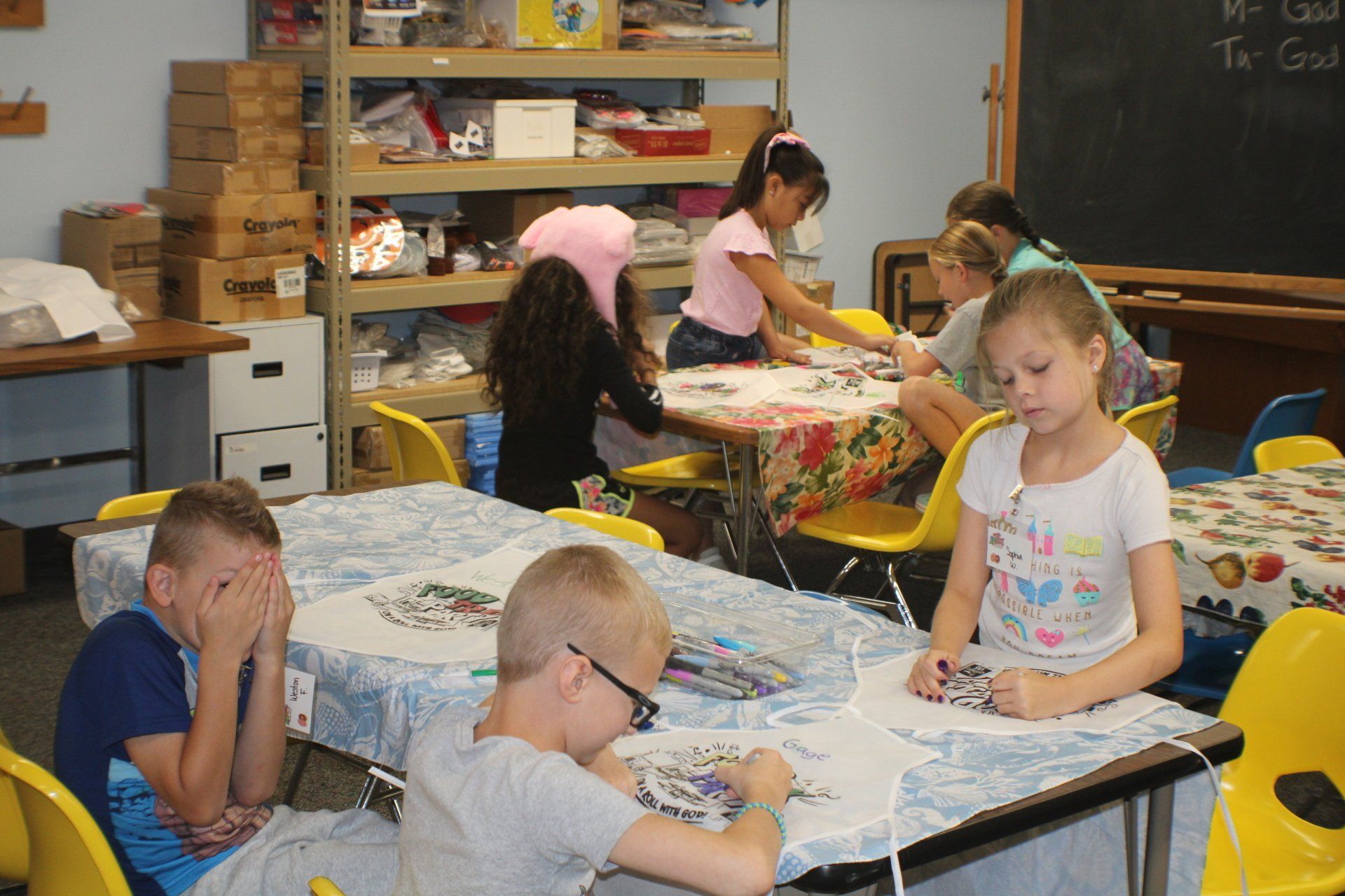Students working at tables in a classroom, drawing and reading together.