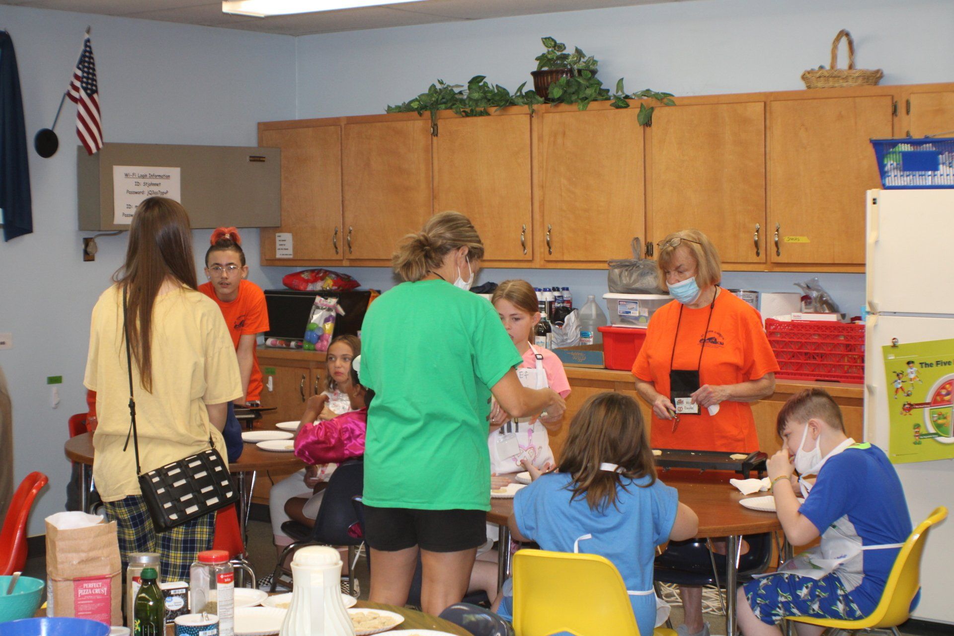People gathered in a classroom around tables, working and talking near a counter and cabinets.
