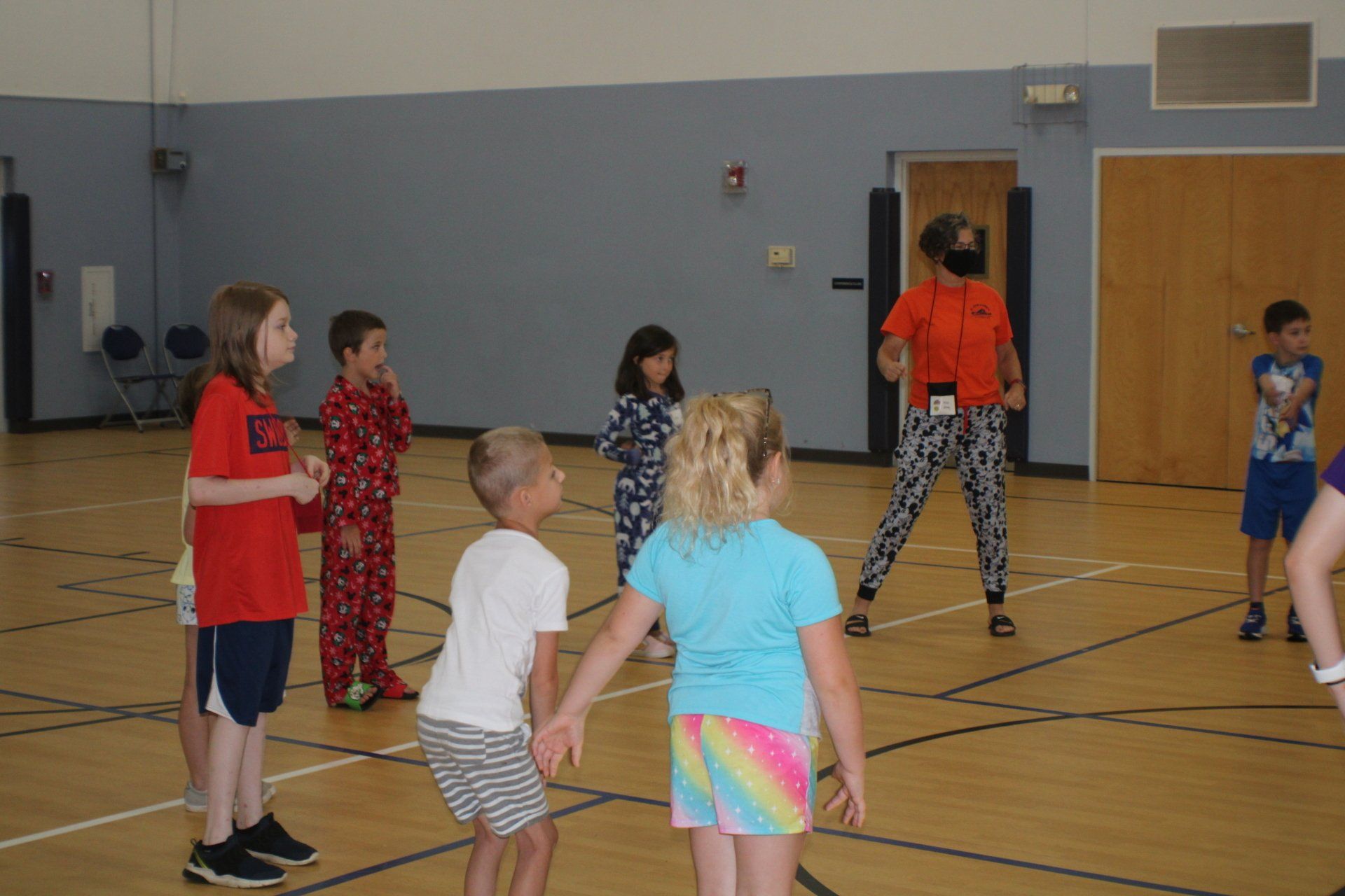 Children playing in a gymnasium, standing in a circle during a game or activity.