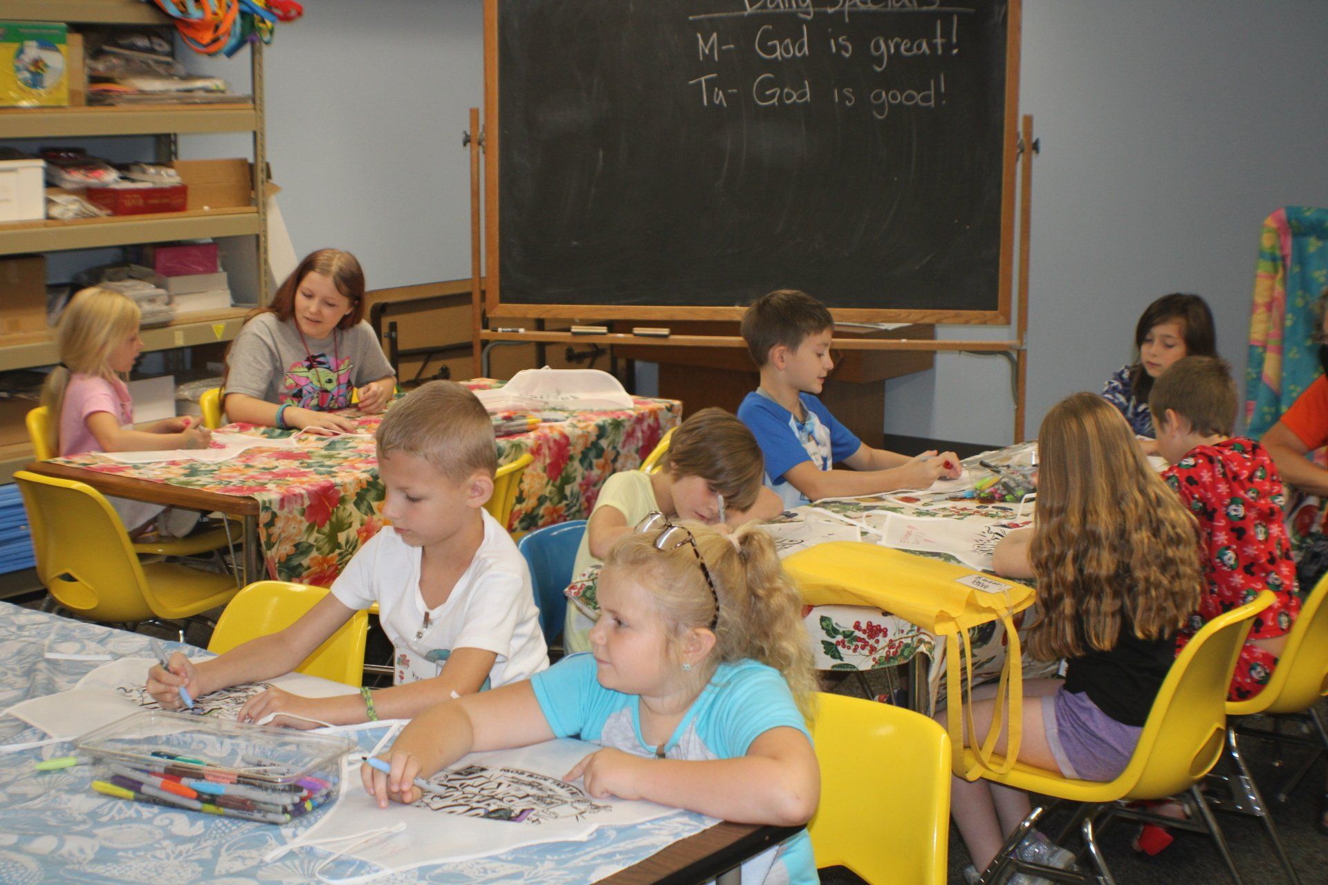 Children seated at desks, working on art projects in a classroom with a chalkboard.